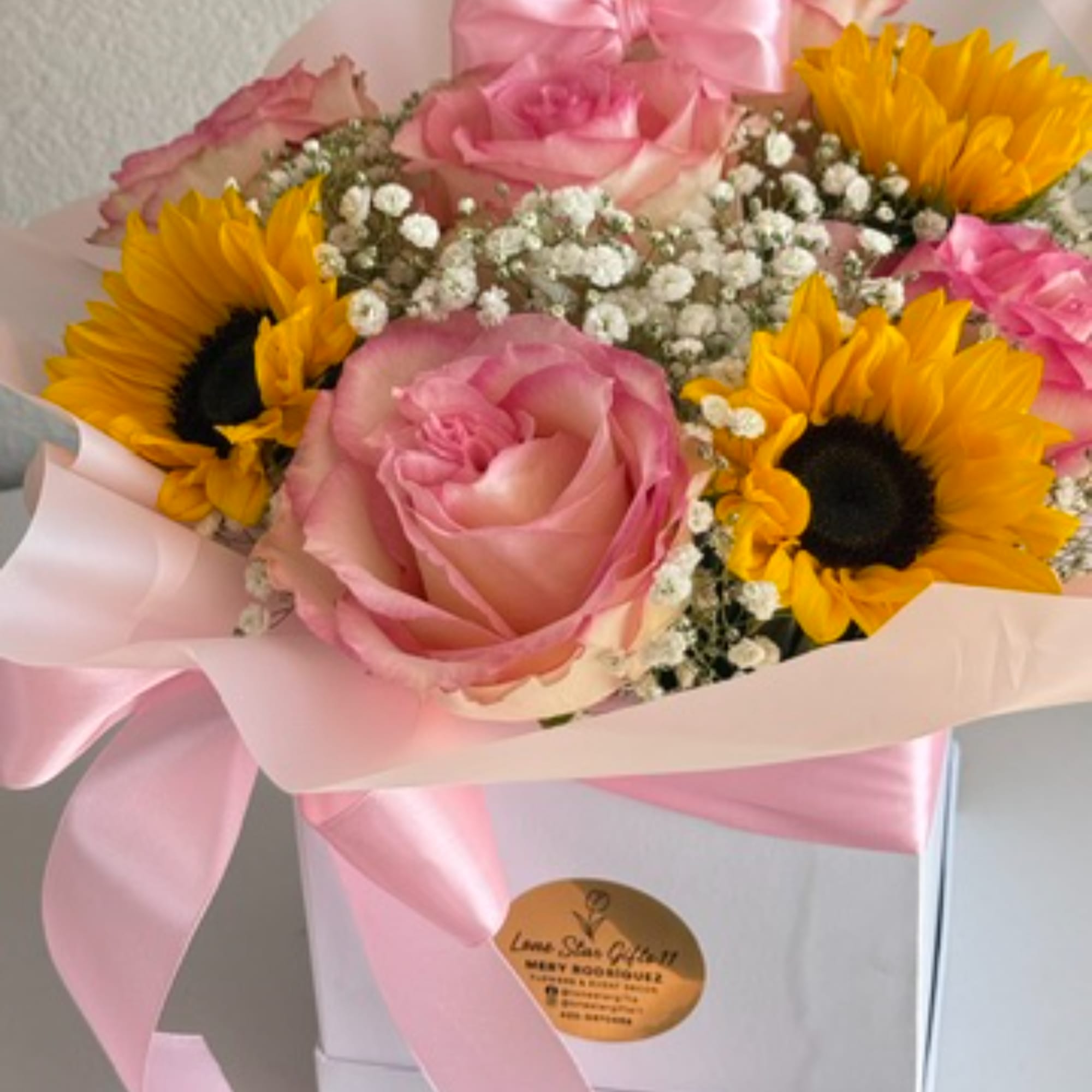 Pink roses and yellow sunflowers arranged in a pink-wrapped box