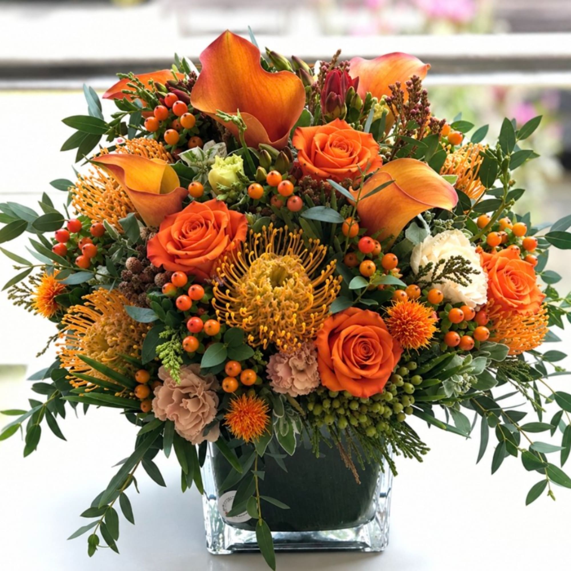 Orange roses and calla lilies in a clear square vase