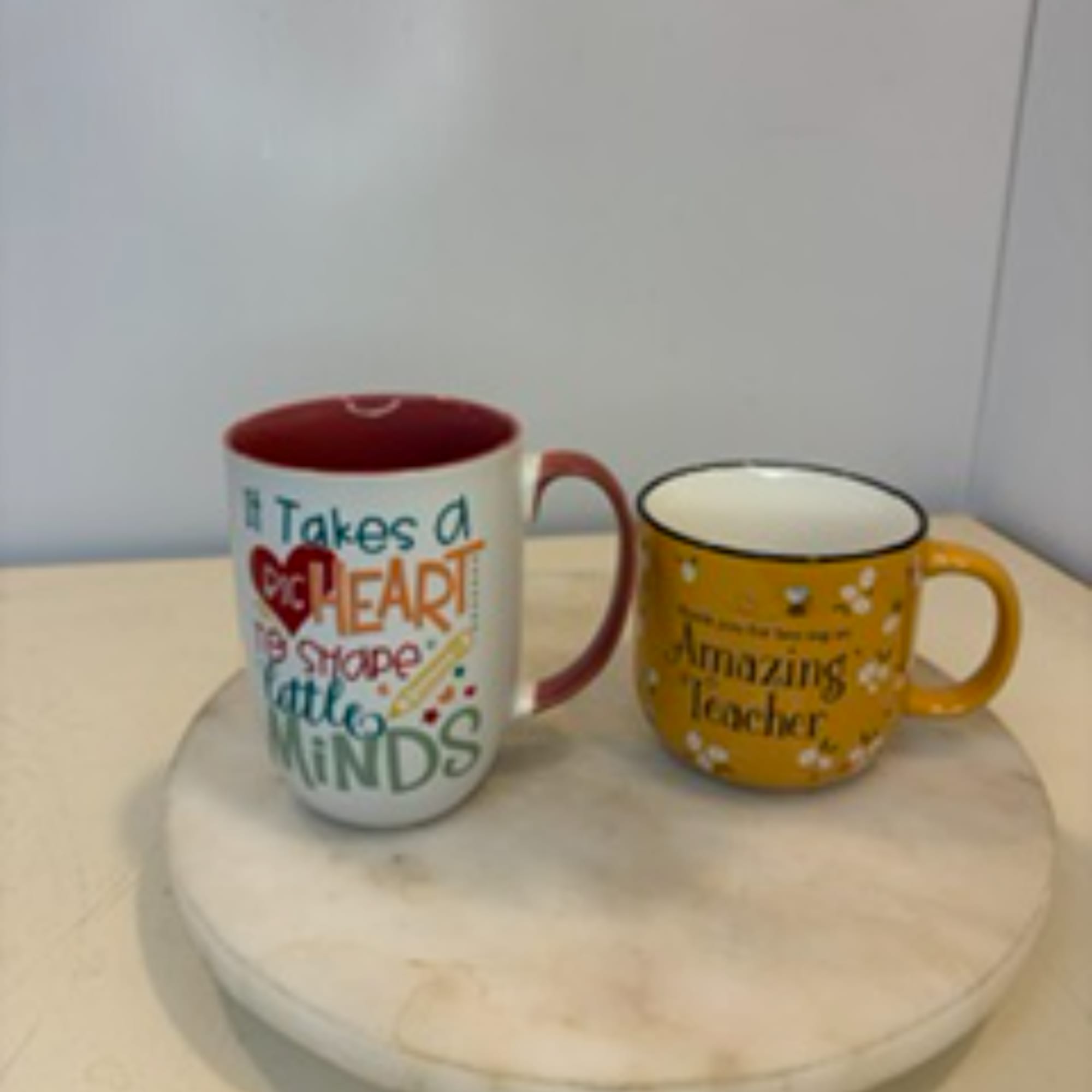 Two printed ceramic mugs on a round tray, one white and one yellow.