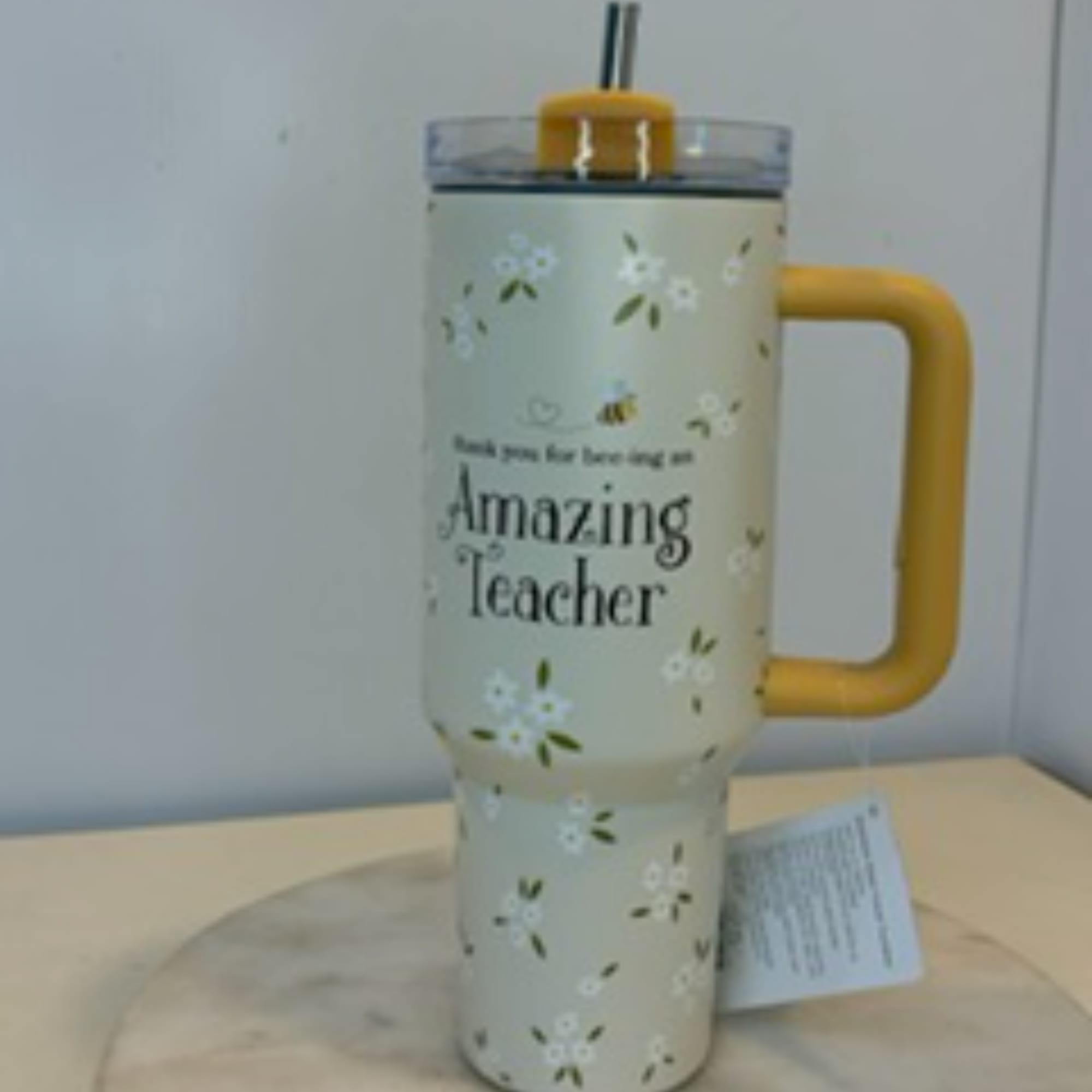 Floral-patterned travel tumbler with a yellow handle and "Amazing Teacher" text