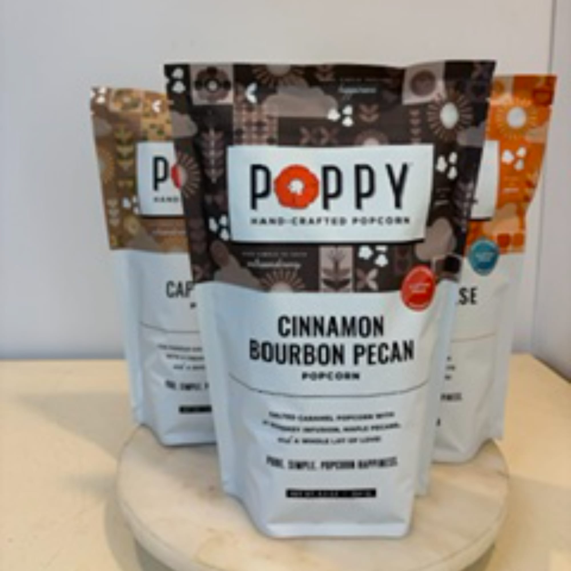 Three bags of Poppy hand-crafted popcorn on a round display stand