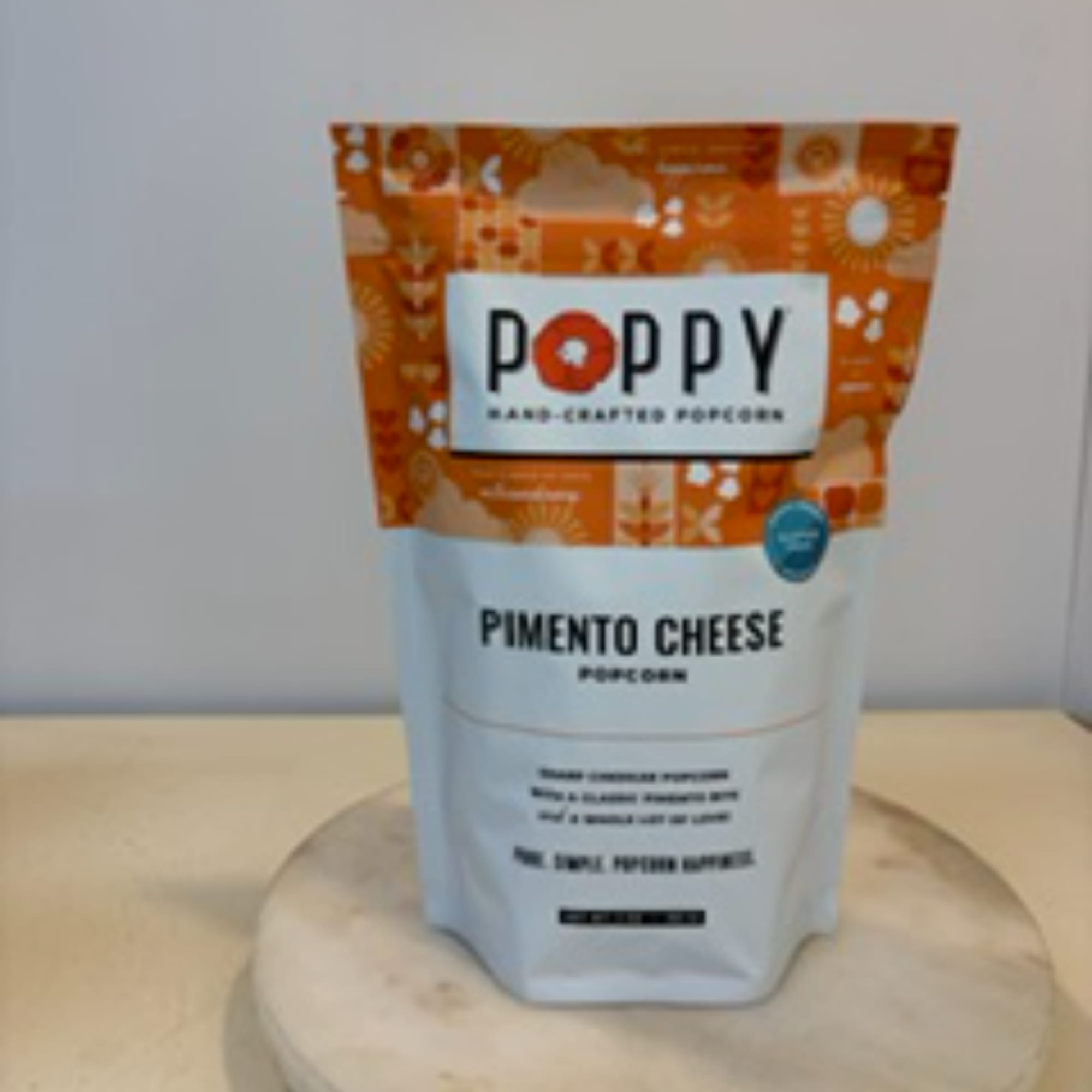 Bag of Poppy pimento cheese popcorn on a round stand