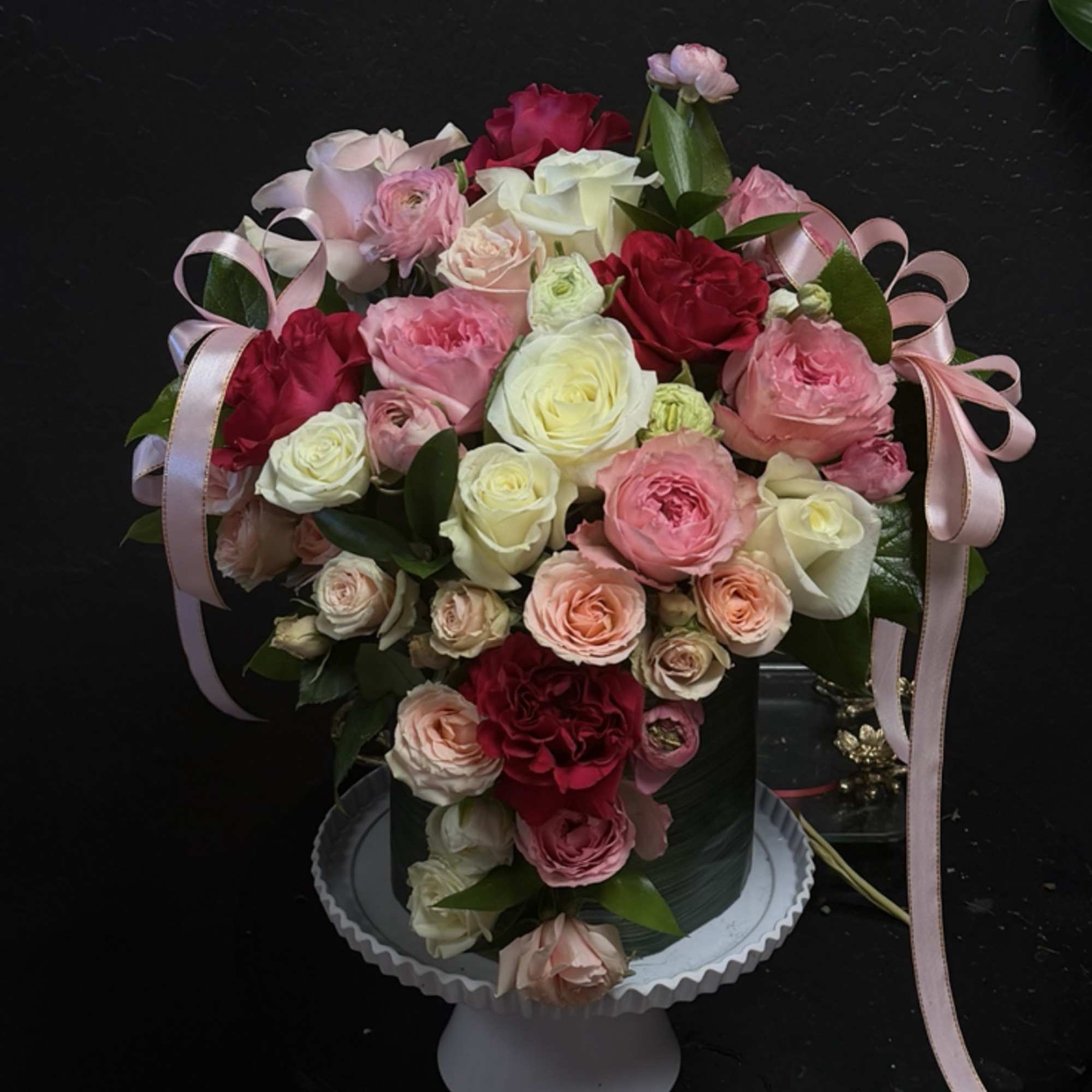 Pink and white rose arrangement in a black vase with ribbon bows