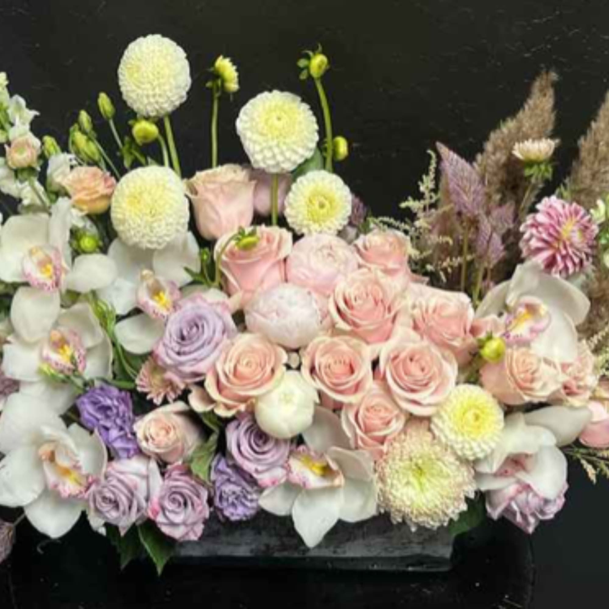 Pastel bouquet with roses, orchids, and round white blooms in a low container