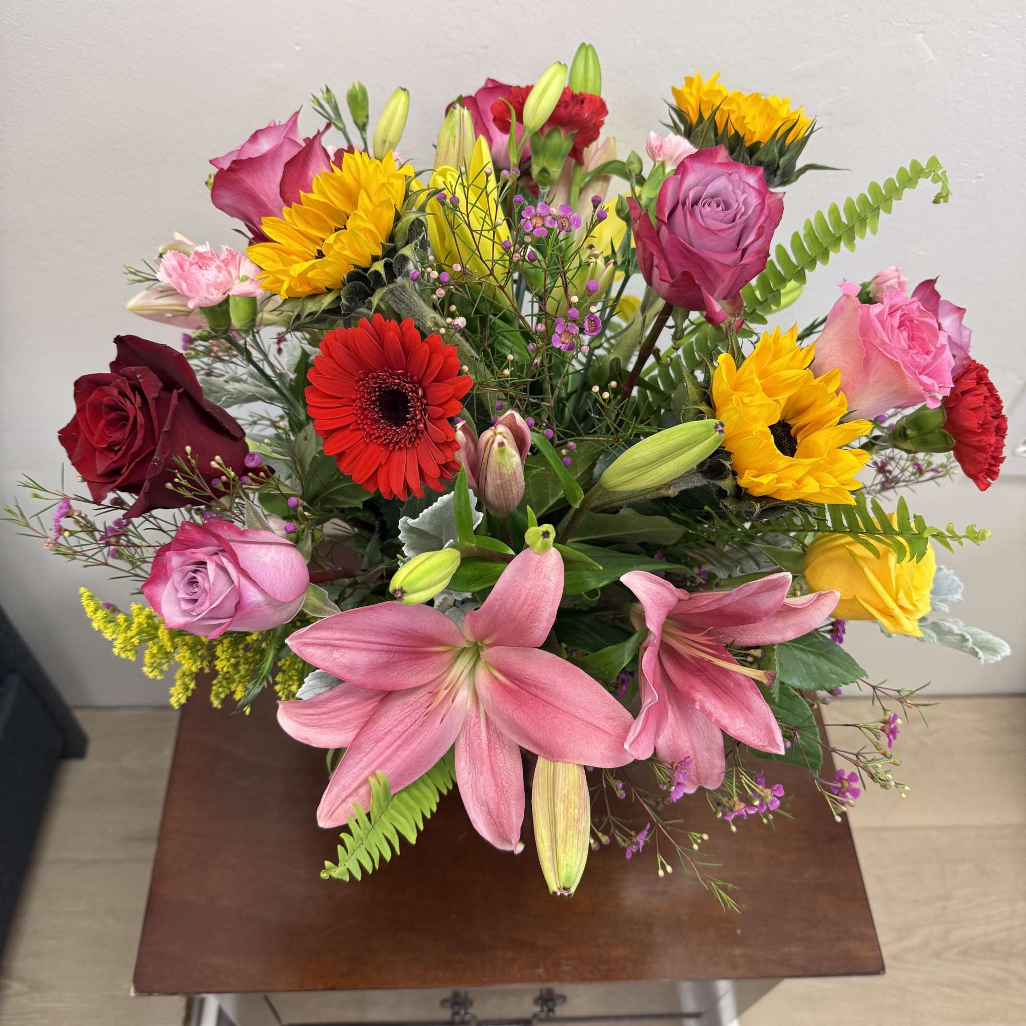Mixed bouquet with pink roses, sunflowers, lilies, and a red gerbera daisy