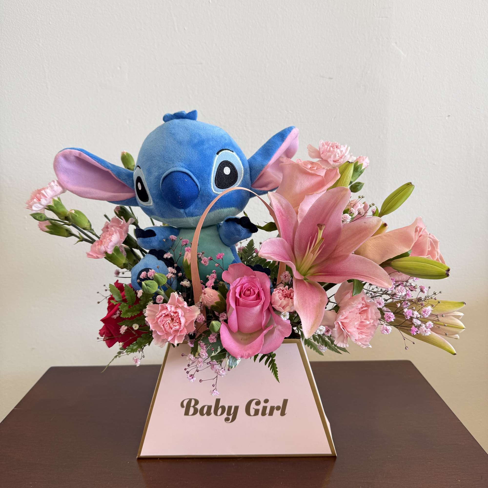Pink floral arrangement with plush blue character toy in a Baby Girl box.