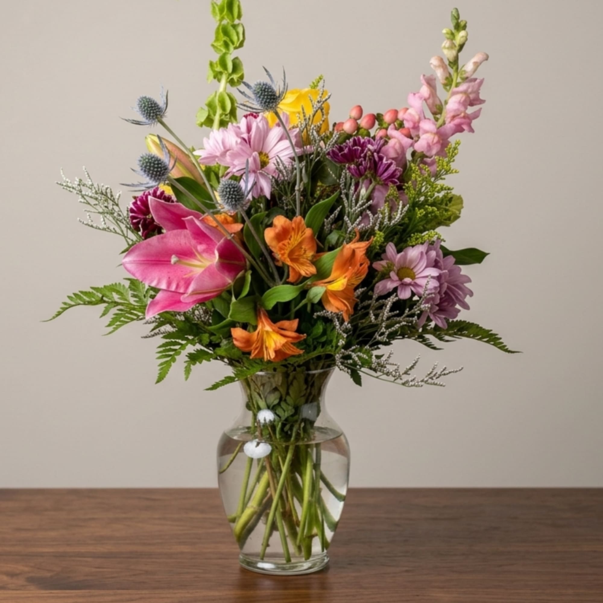 Mixed bouquet of pink, orange, and purple flowers in a clear glass vase