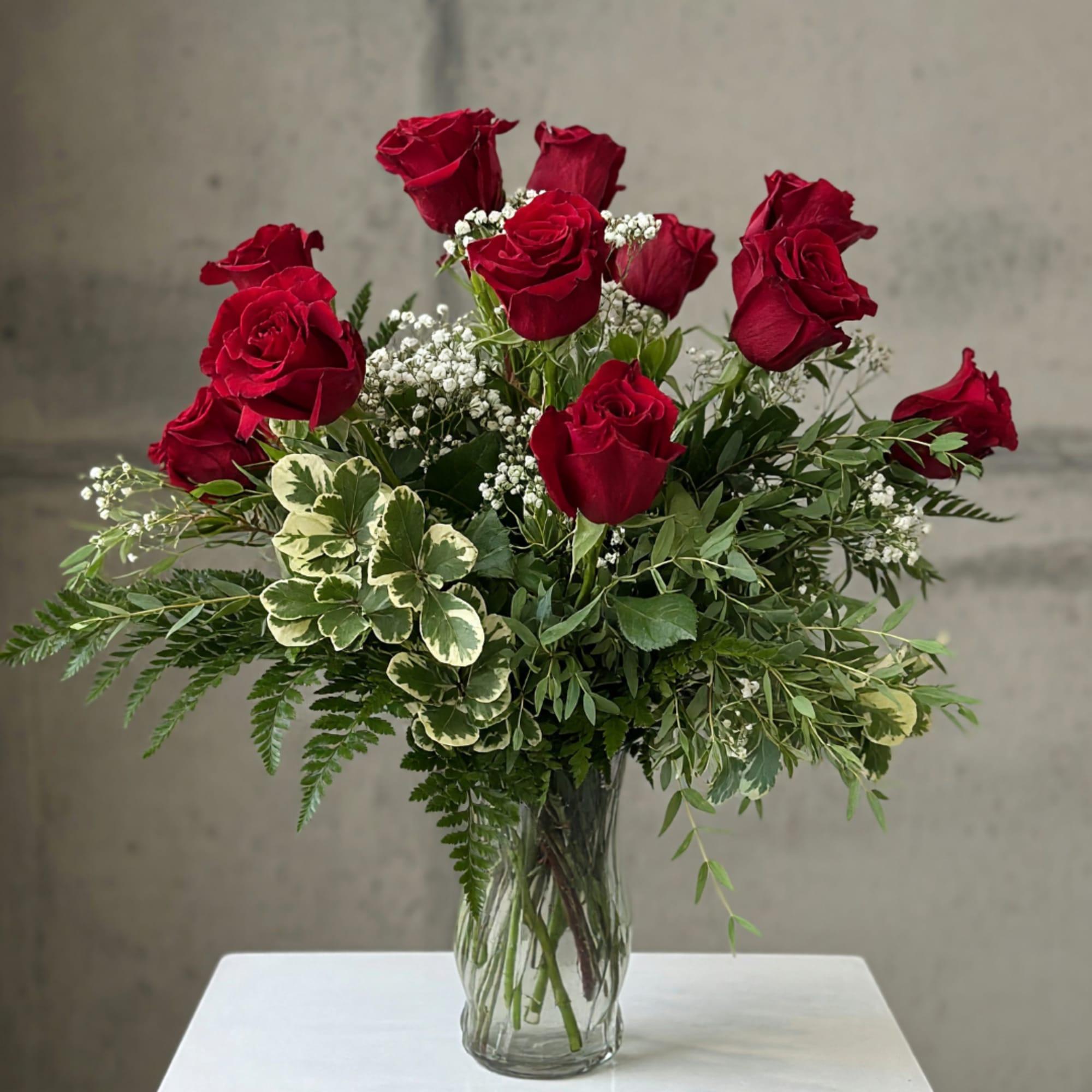 Red roses arranged in a clear glass vase with mixed greenery