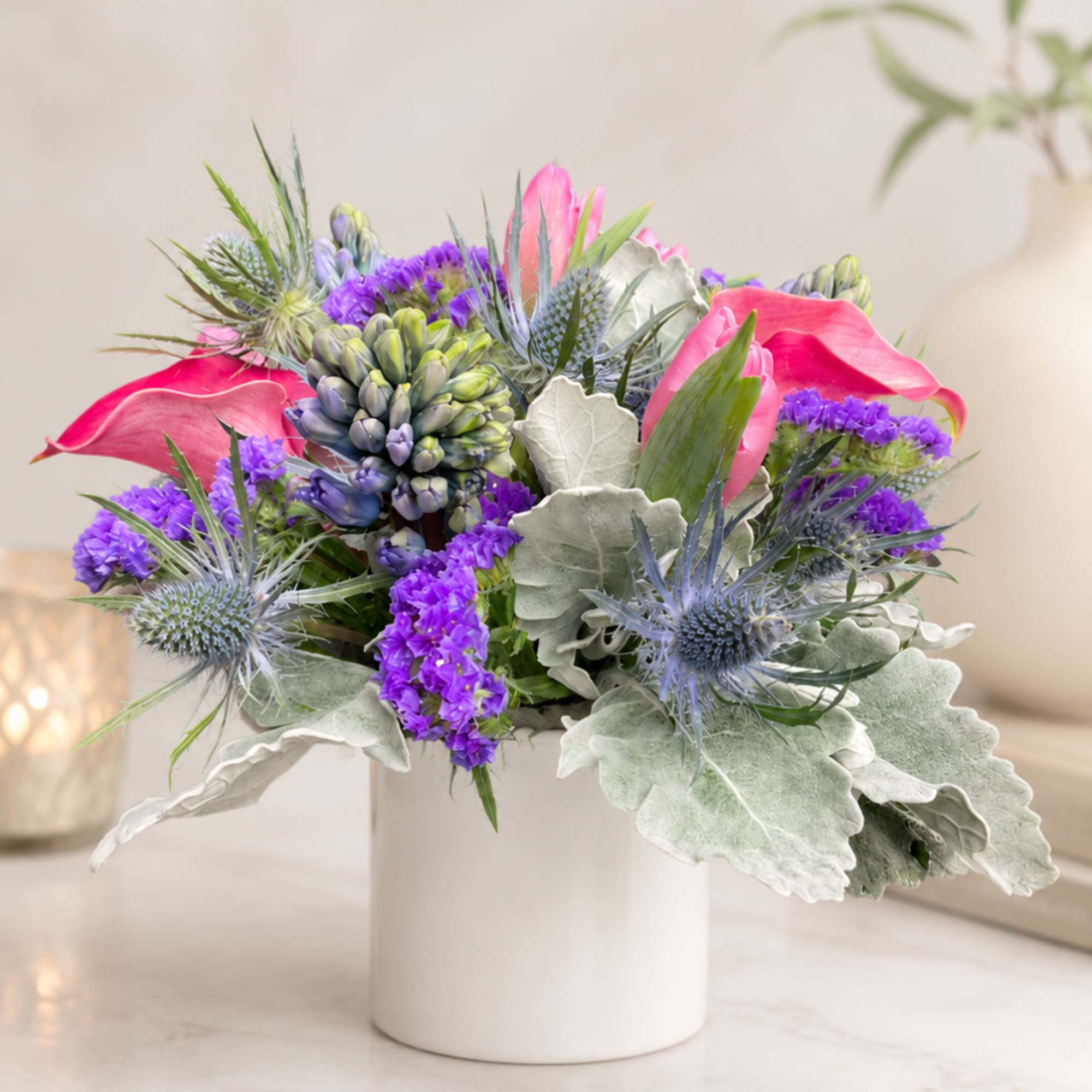 Pink calla lilies and purple thistle in a white vase
