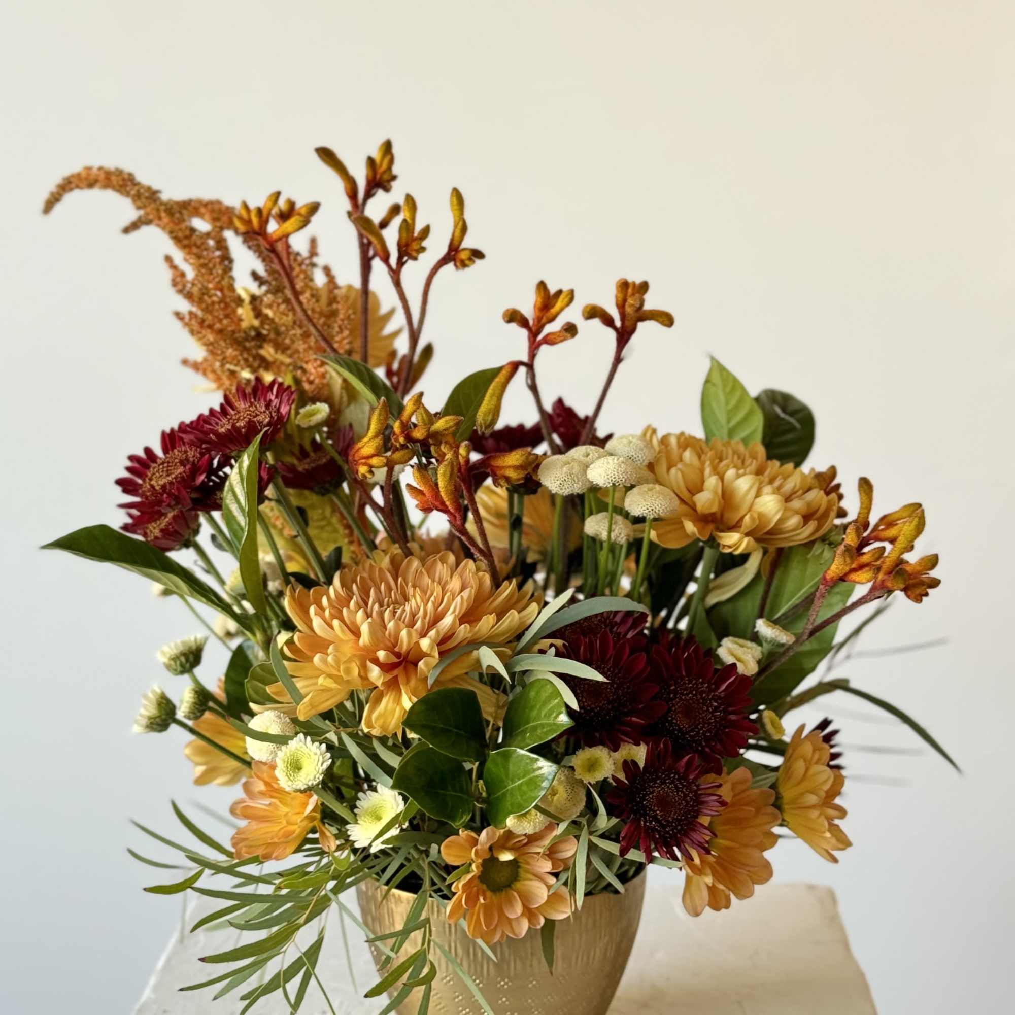 Autumn flower arrangement in a gold vase with orange and burgundy blooms