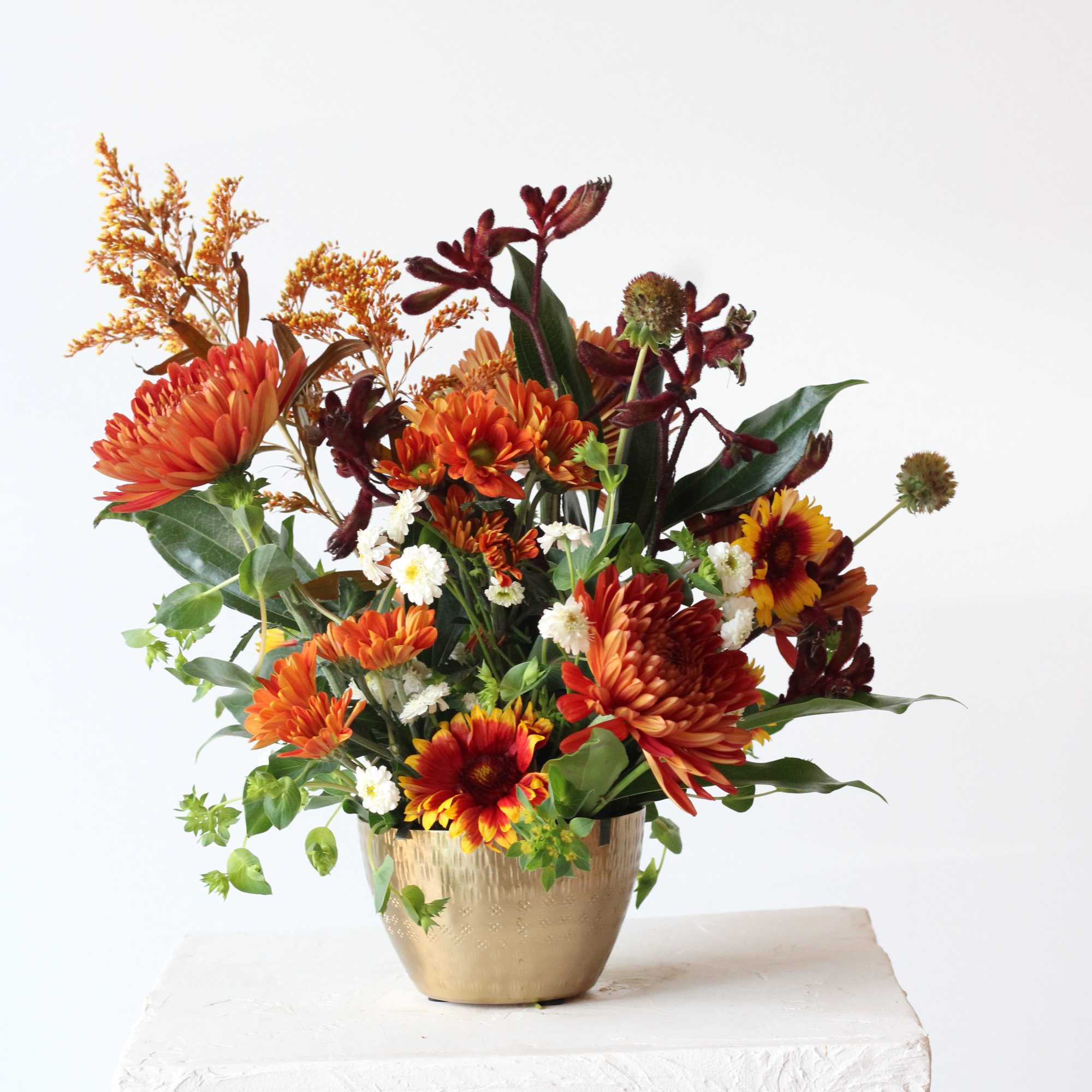 Orange and red mixed flower arrangement in a gold vase