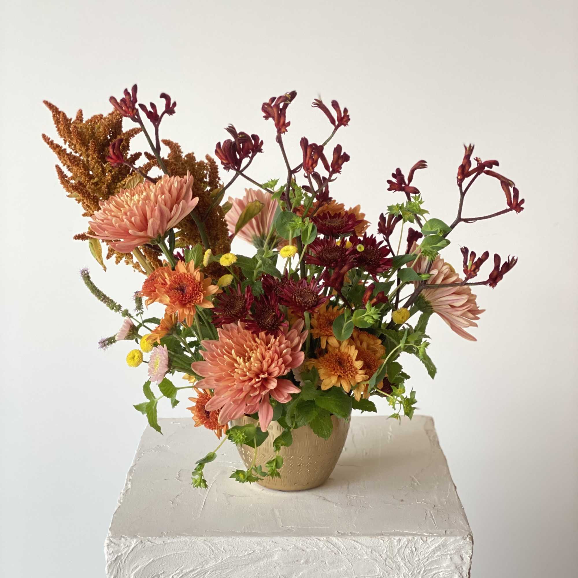 Mixed bouquet of chrysanthemums and small accent flowers in a beige vase