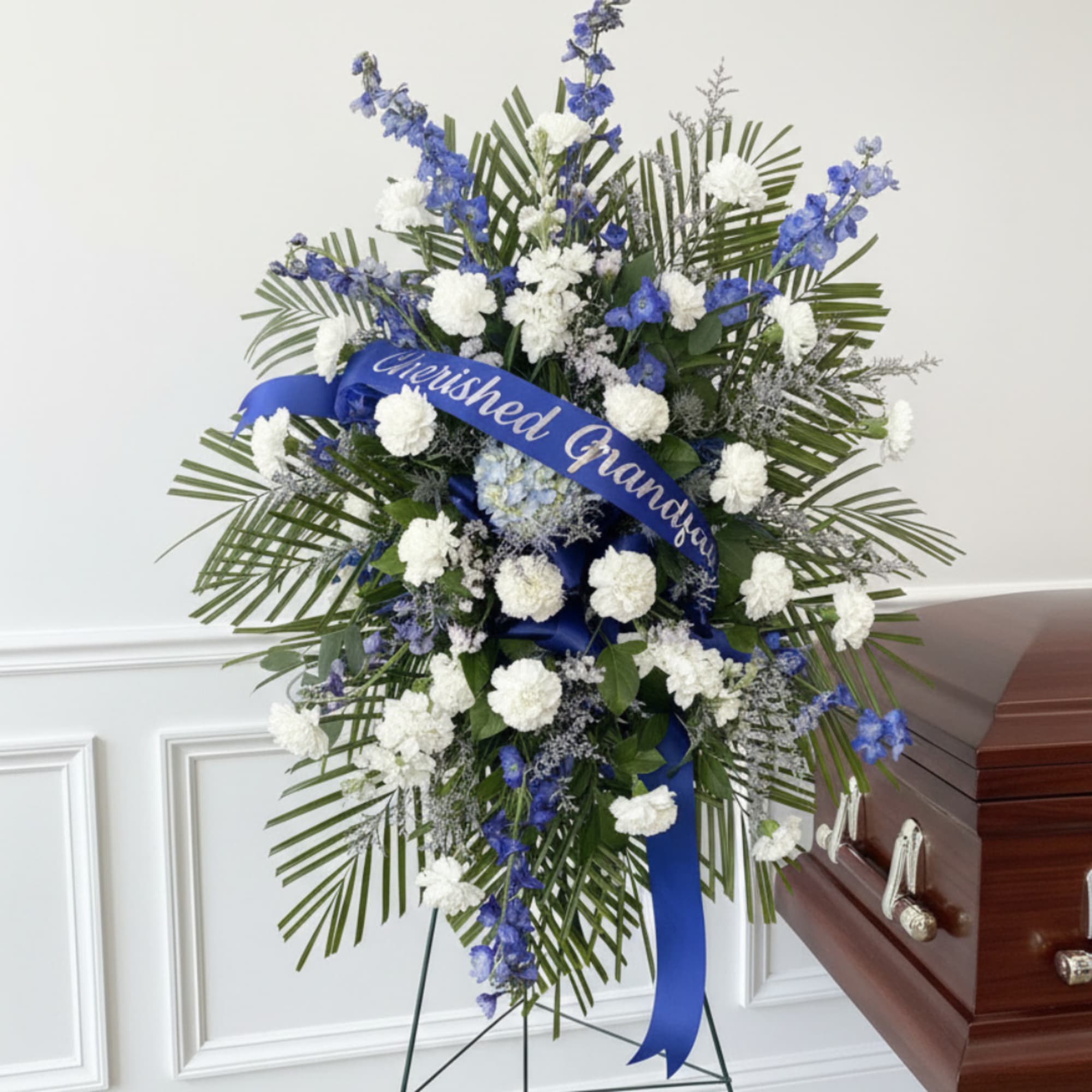 Blue and white funeral spray on an easel beside a casket