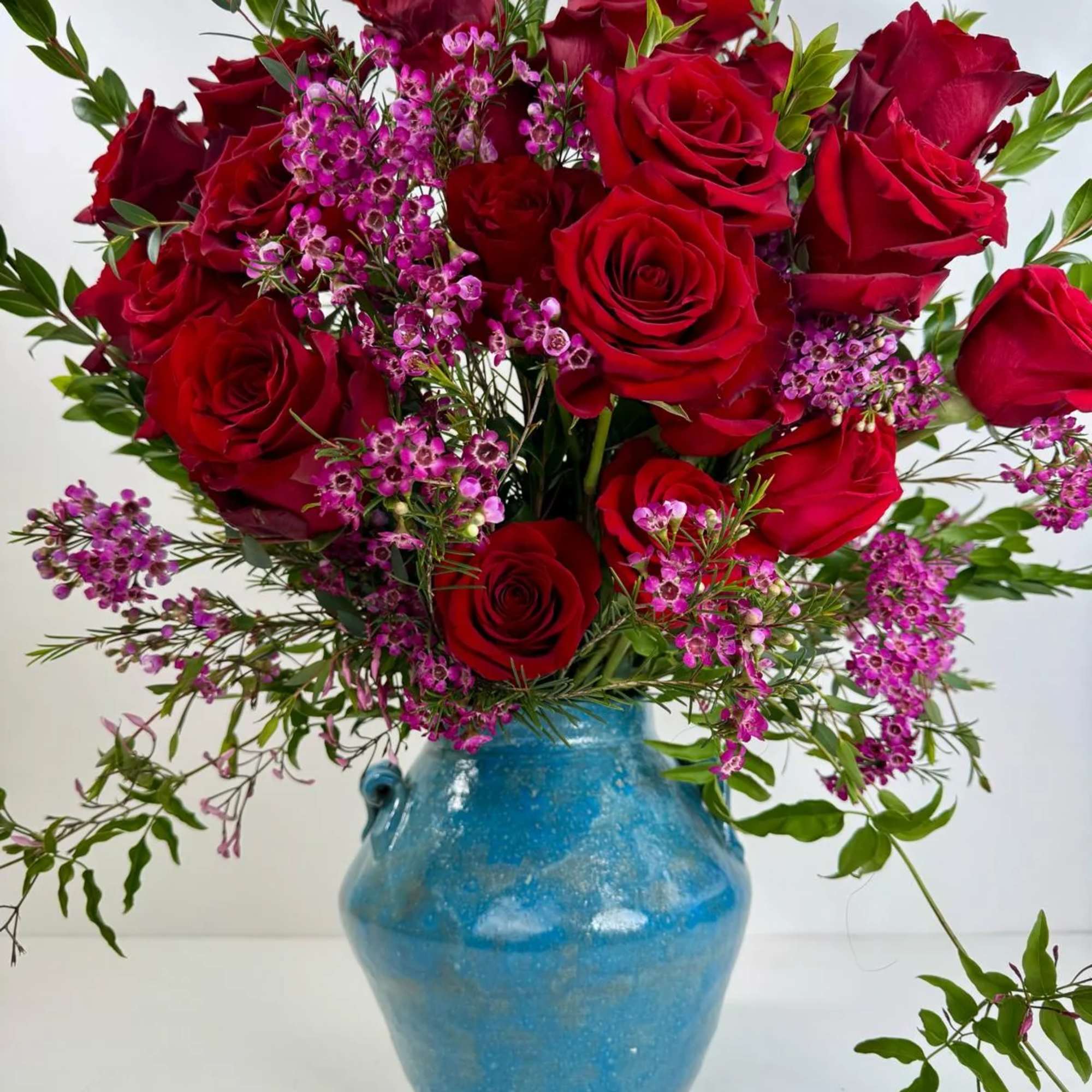 Red roses and purple filler flowers in a blue ceramic vase