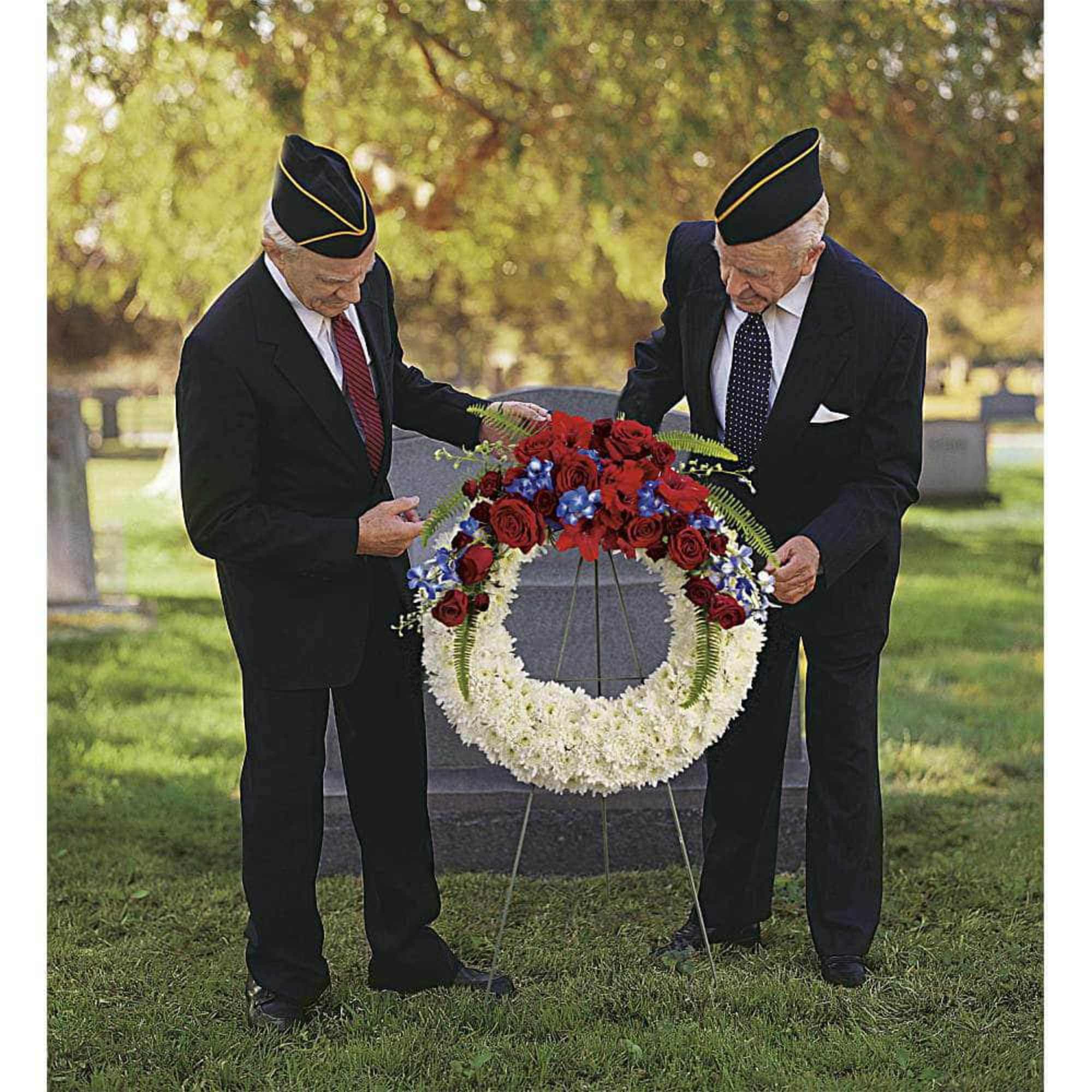 Two men in suits place a floral wreath on a stand outdoors