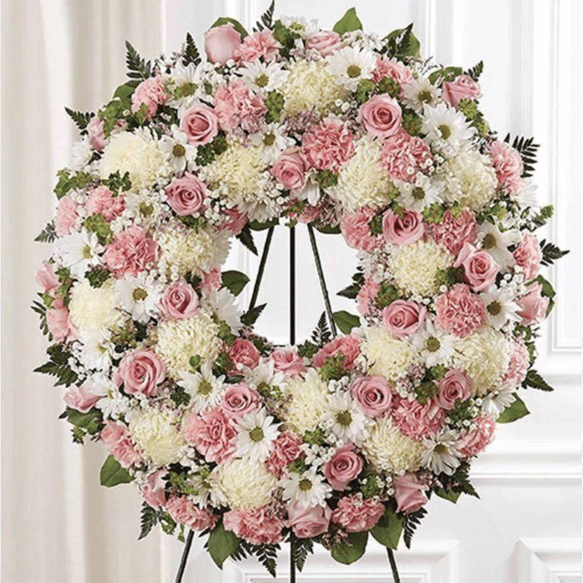 Pink and white floral wreath on a black stand