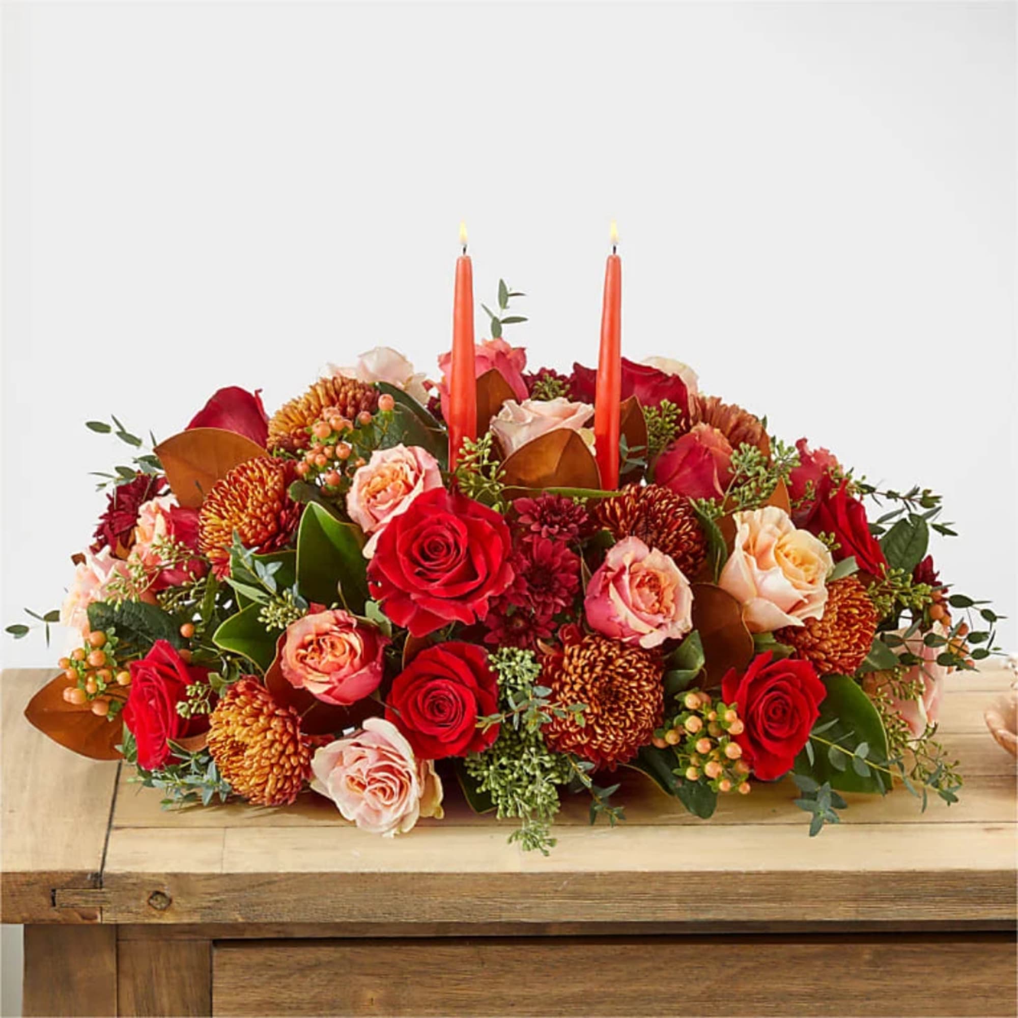 Low floral centerpiece with red and peach roses and two orange candles