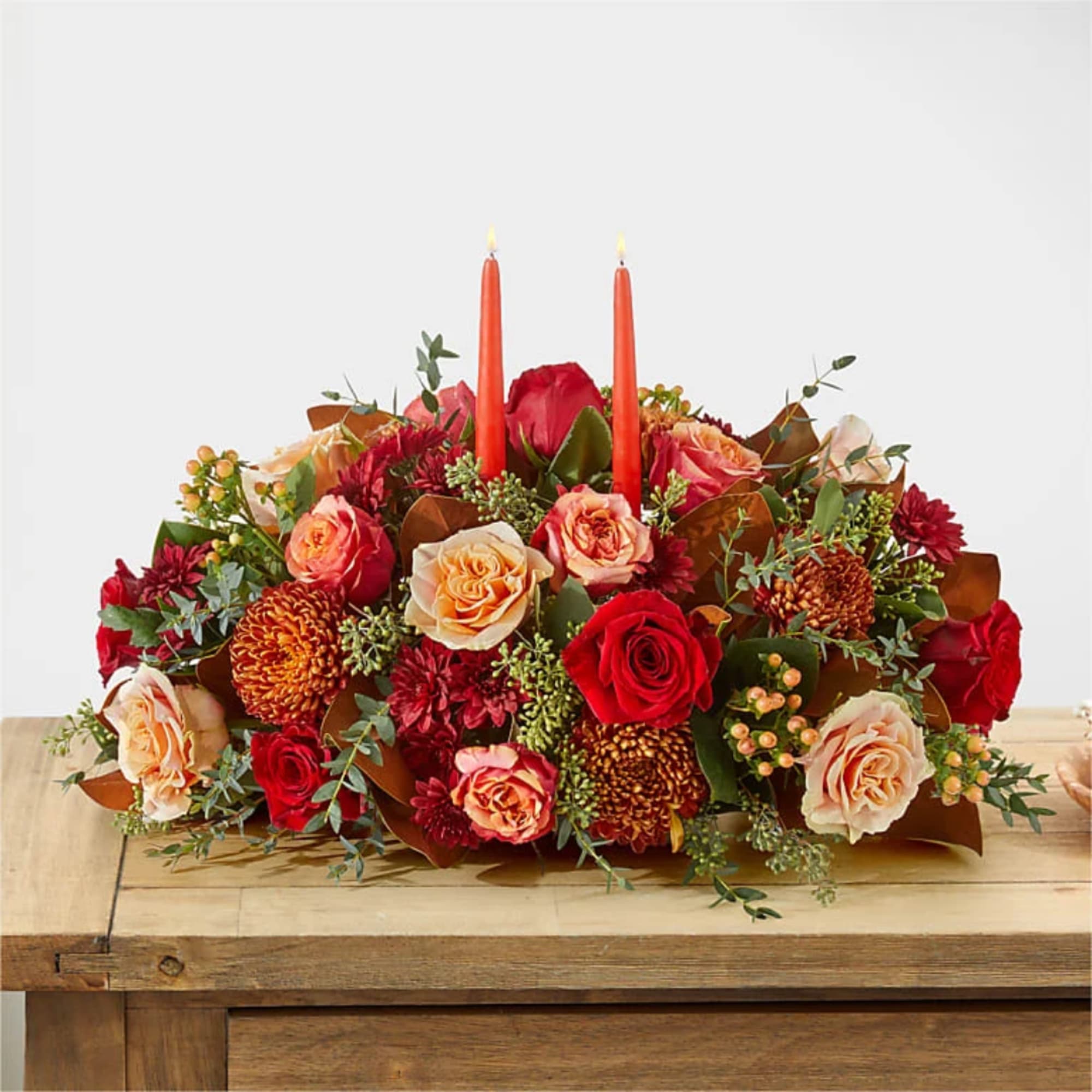 Low floral centerpiece with red and peach roses and two orange candles