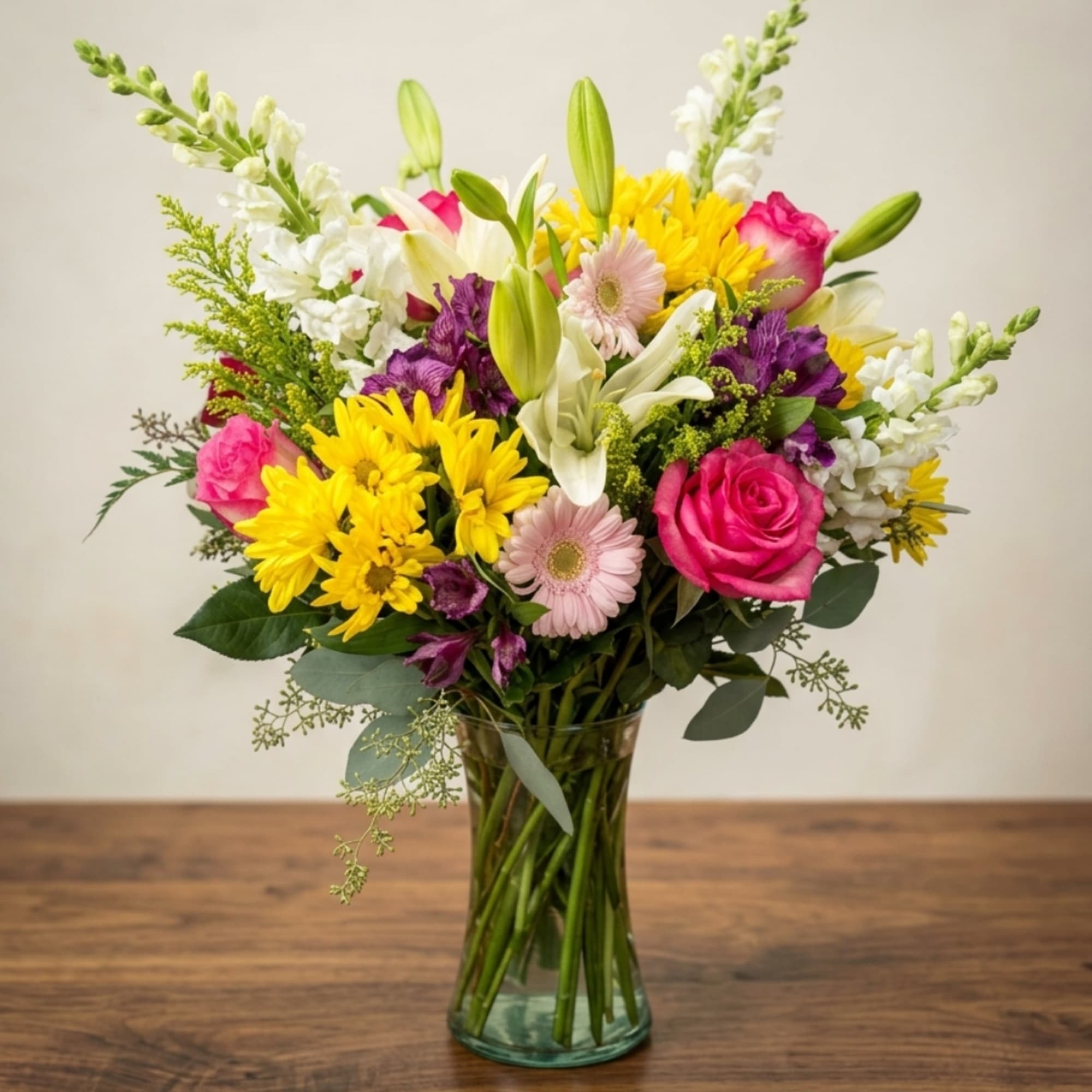 Mixed bouquet of pink, yellow, white, and purple flowers in a glass vase