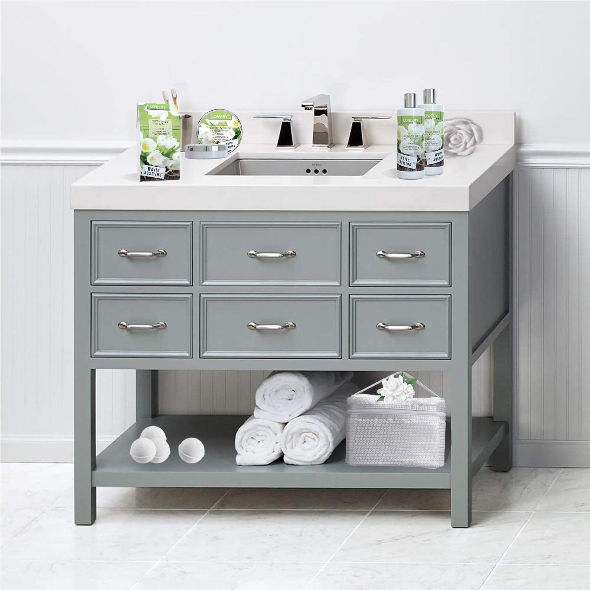 Grey bathroom vanity with white countertop displaying green and white bath products and rolled towels