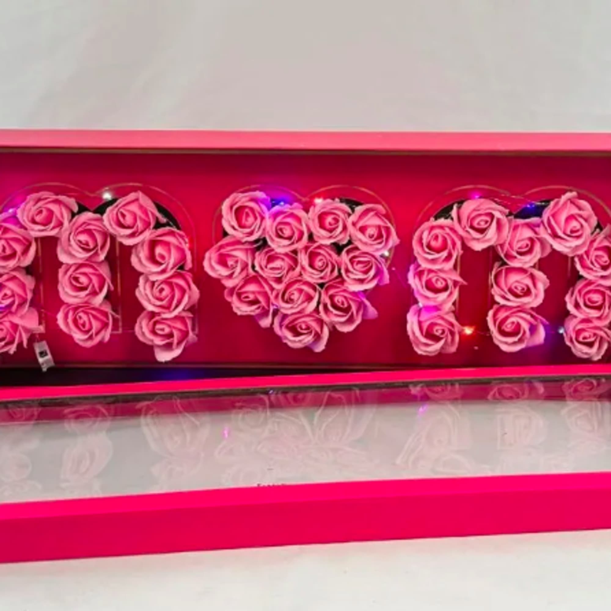 Pink boxed display of artificial pink roses forming letters and a heart shape with tiny lights