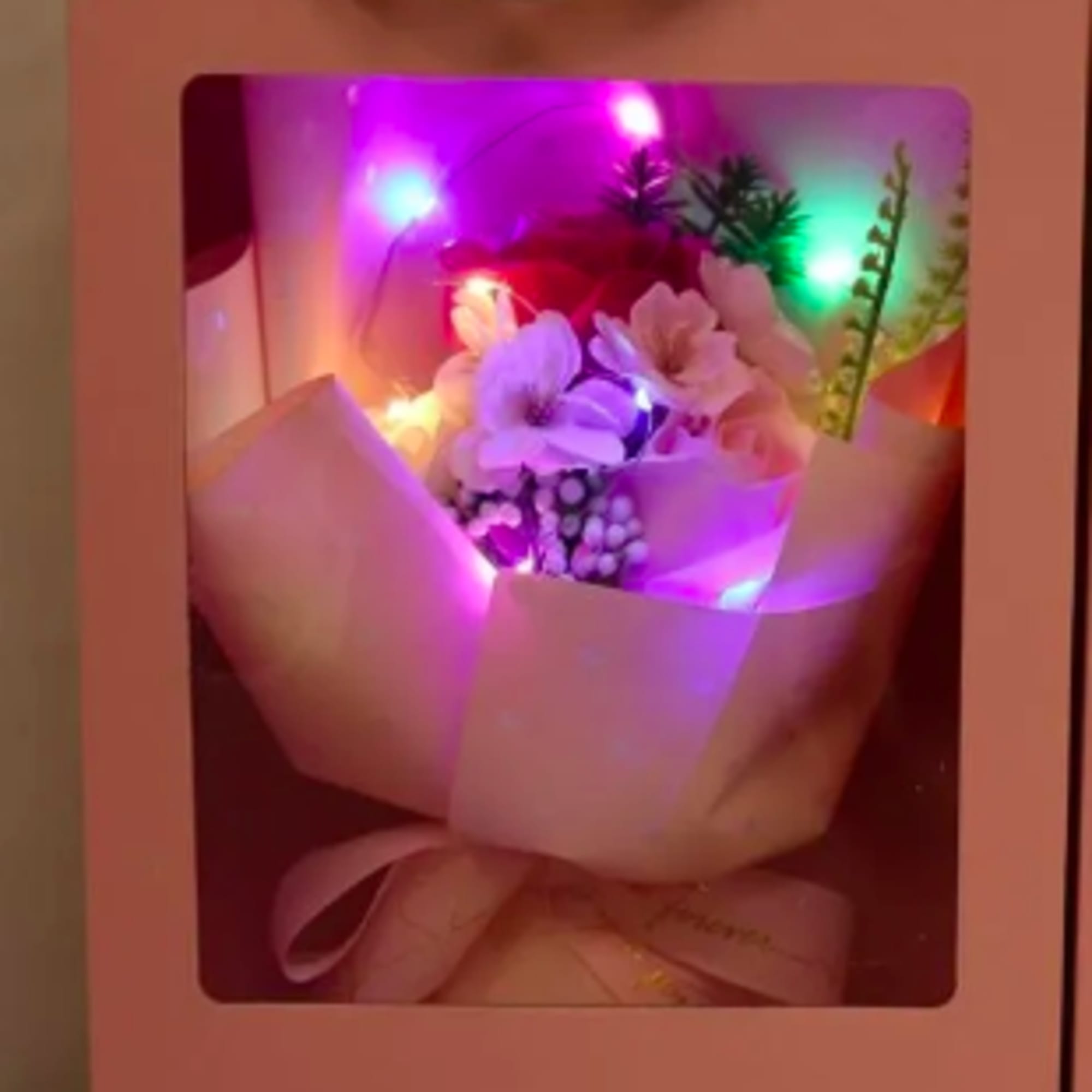 Pink gift box with a small light-up bouquet of pastel flowers seen through a clear window