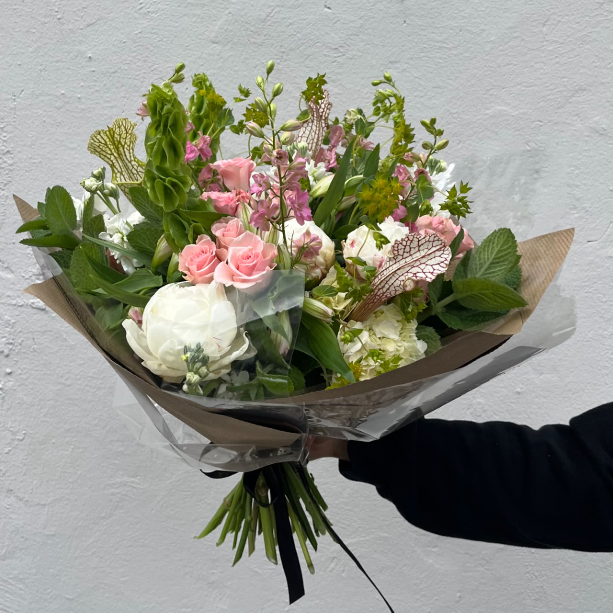 Hand-tied bouquet of pink and white flowers wrapped in brown paper