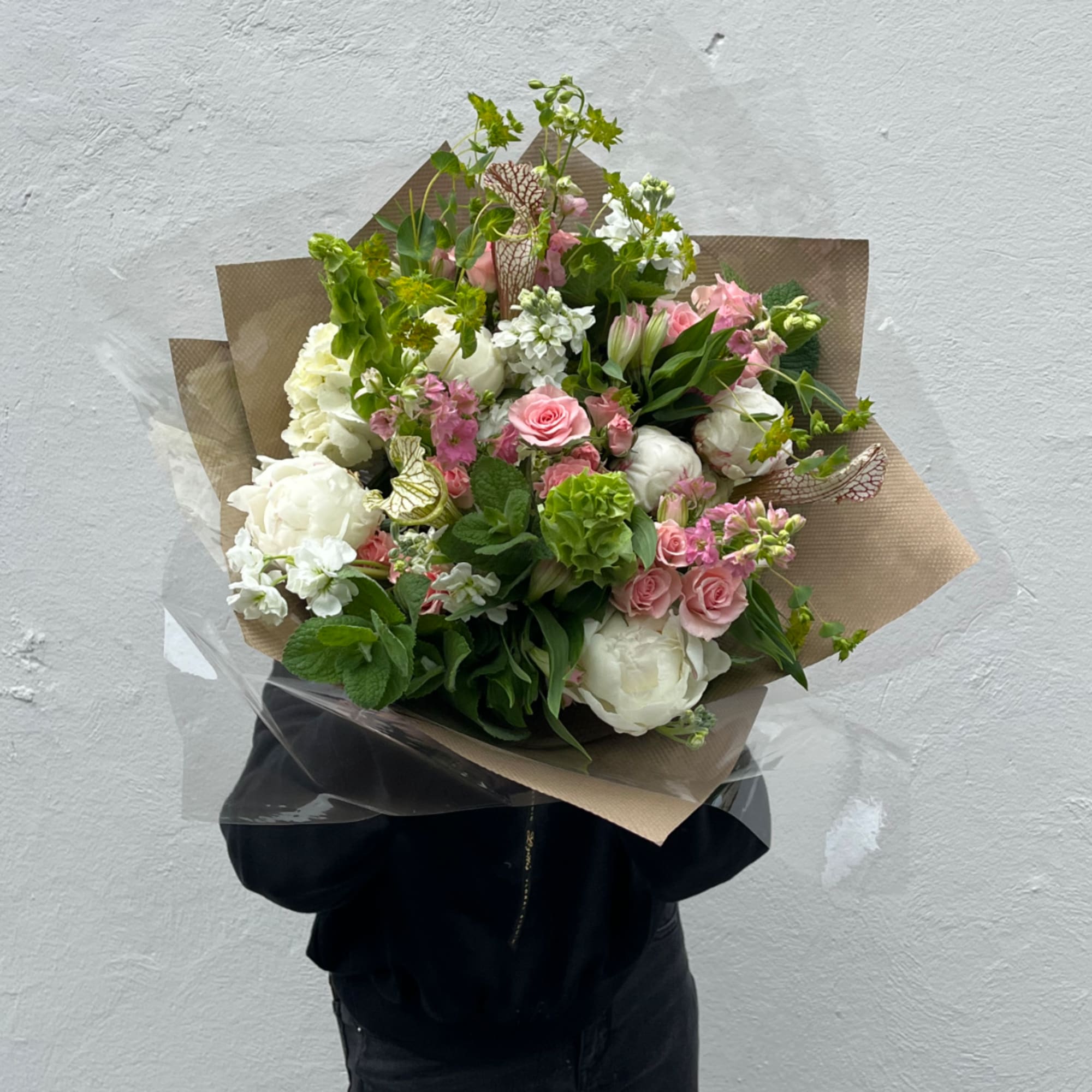 Handheld bouquet of pink and white flowers wrapped in brown paper