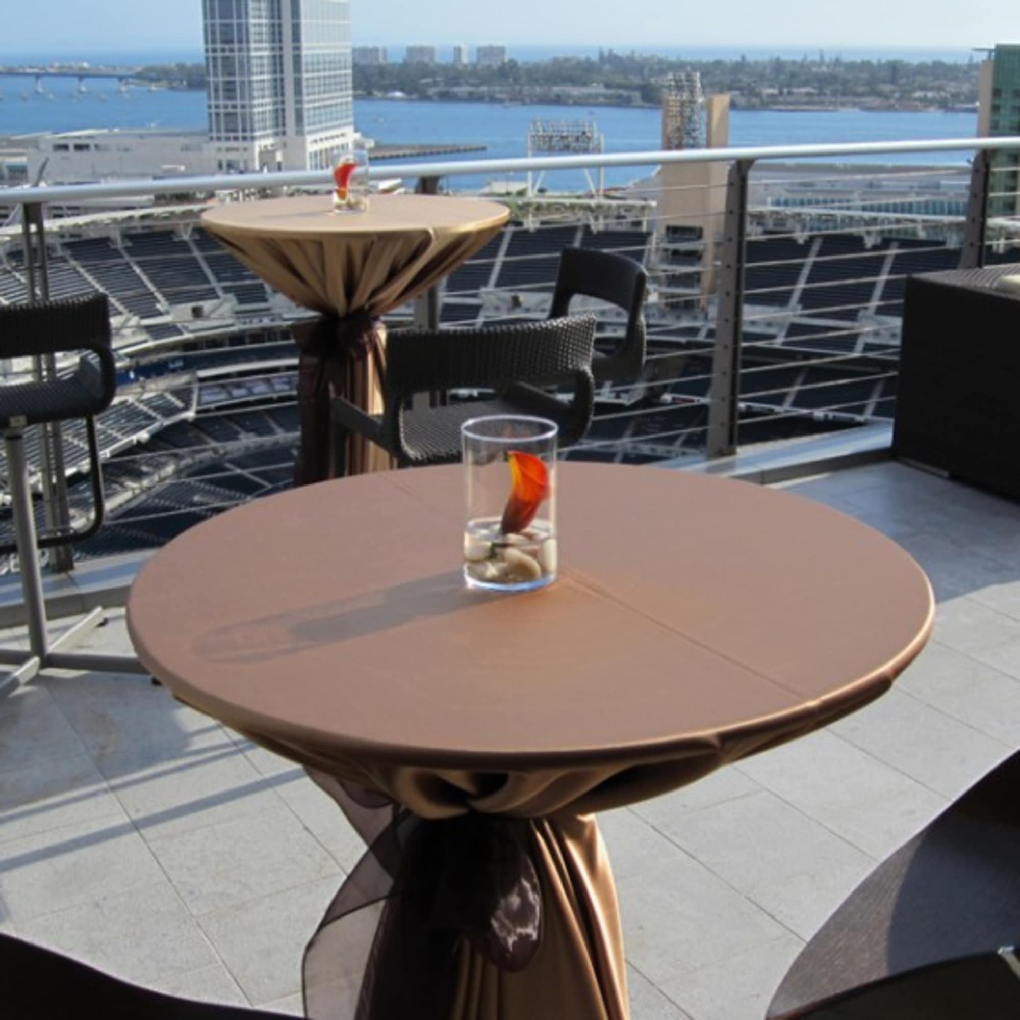 Cocktail tables on a rooftop terrace overlooking a stadium and waterfront