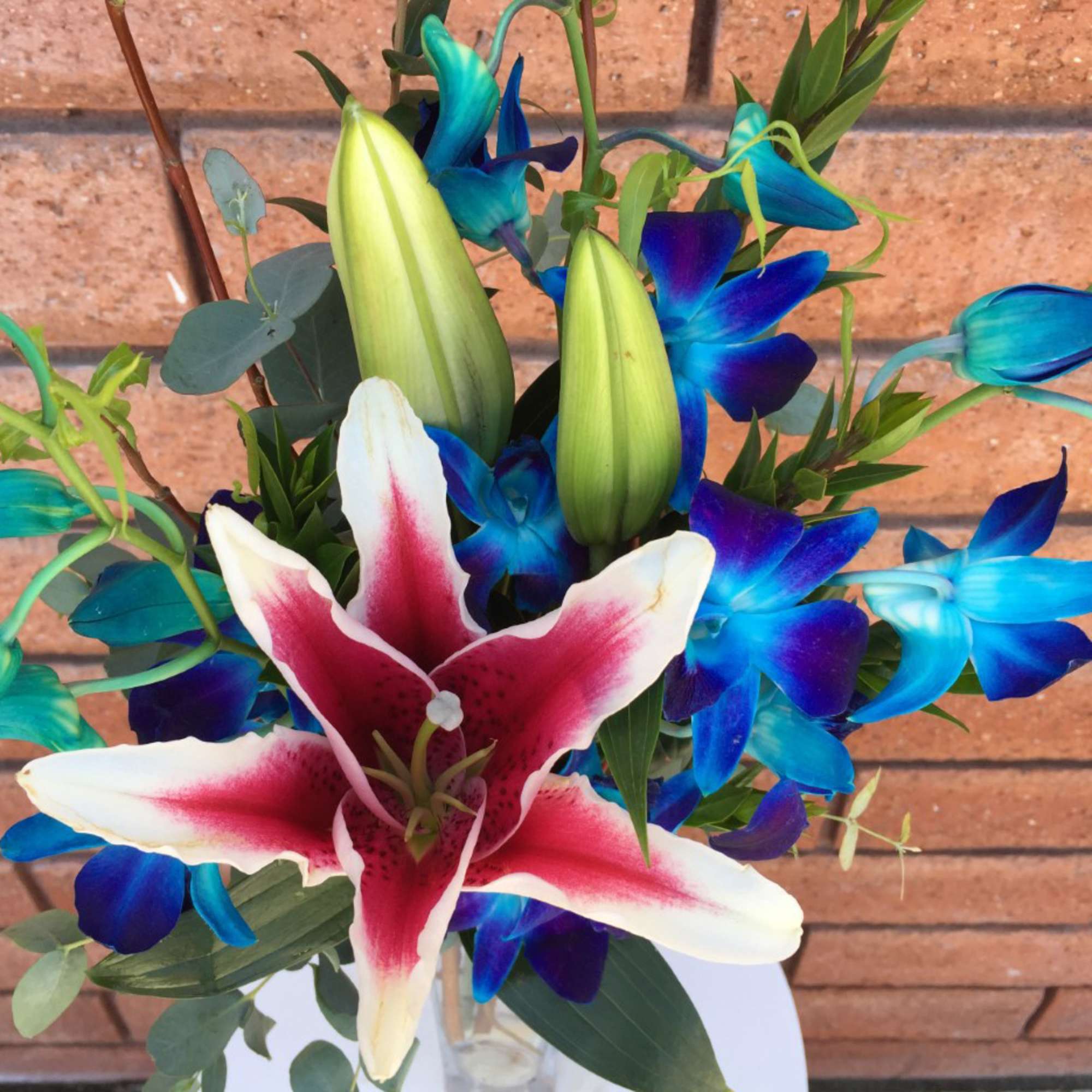 Bouquet with a pink-and-white lily and blue orchids in a glass vase