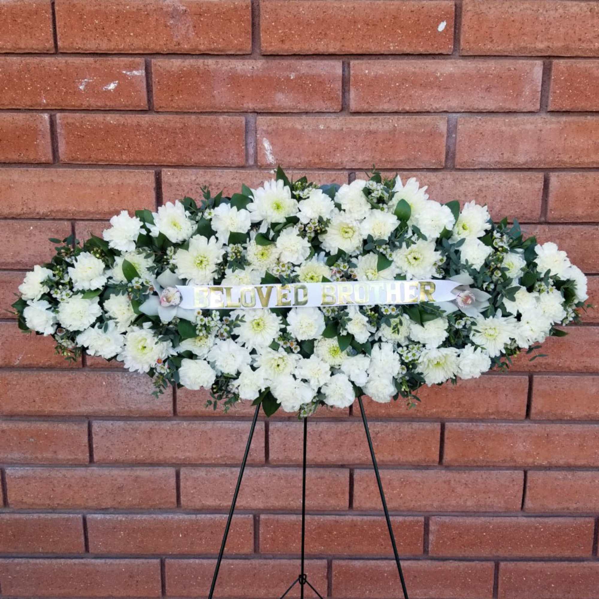 White funeral spray on an easel with a "Beloved Brother" ribbon