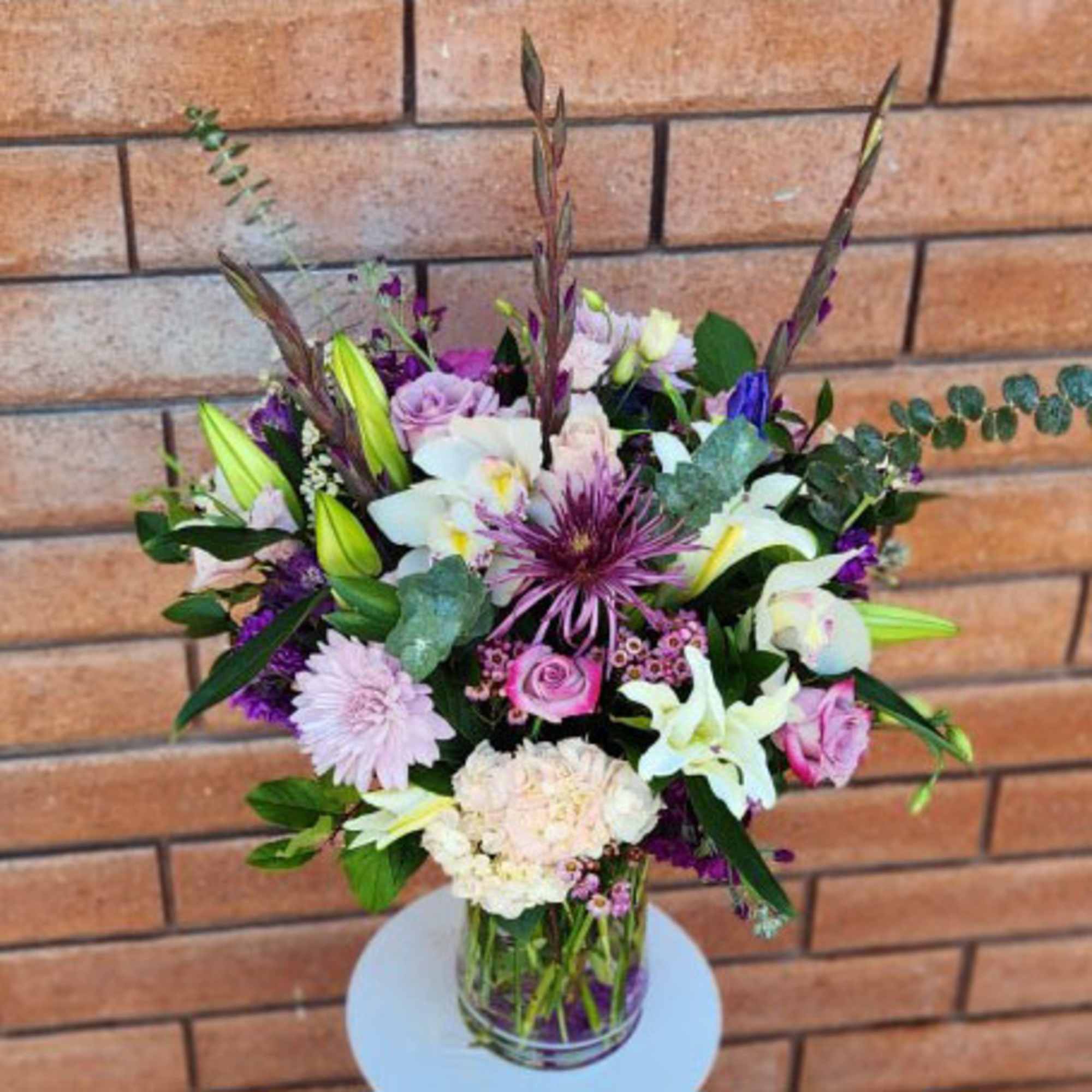 Mixed bouquet of lilies, roses, and purple flowers in a glass vase