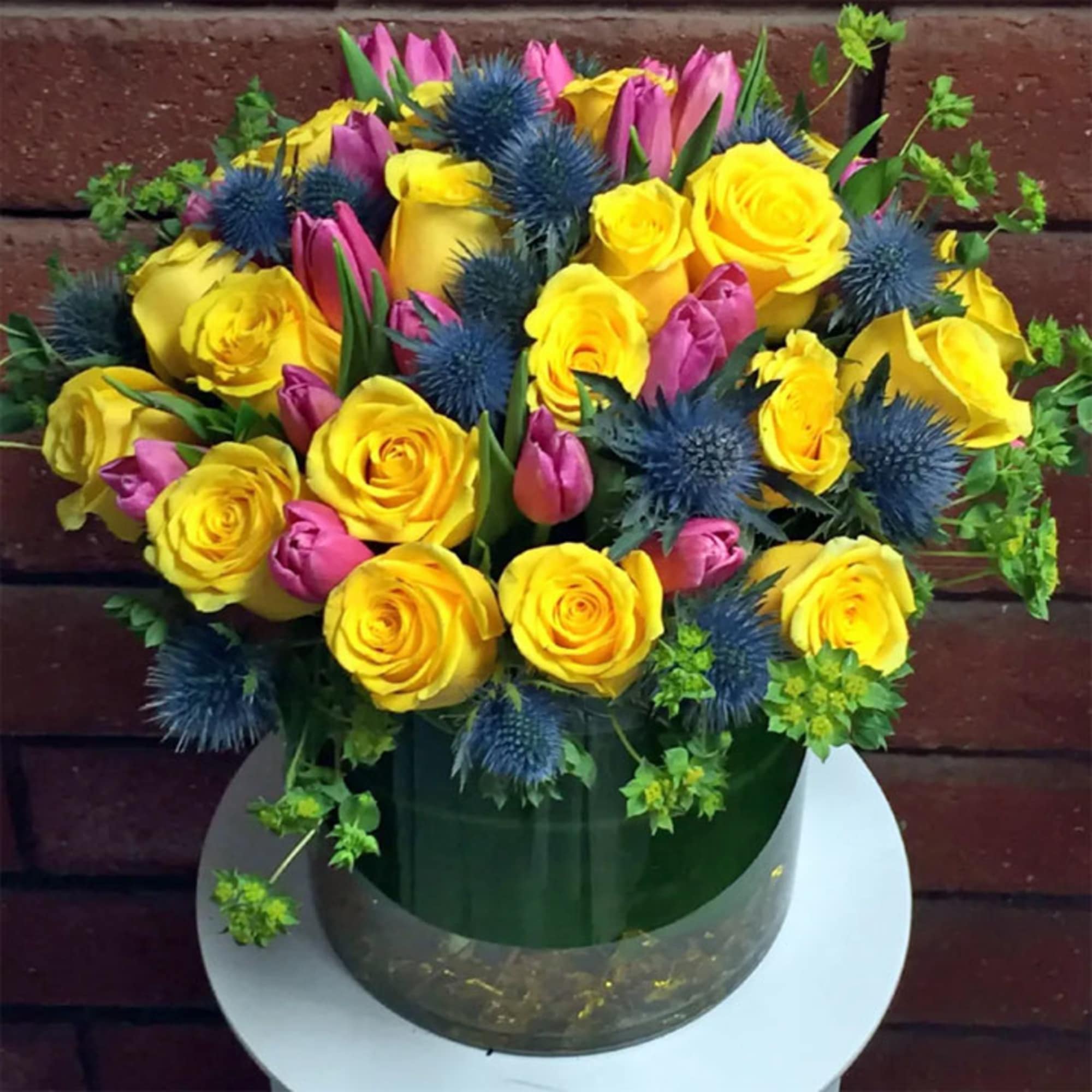 Bouquet of yellow roses, pink tulips, and blue thistles in a vase