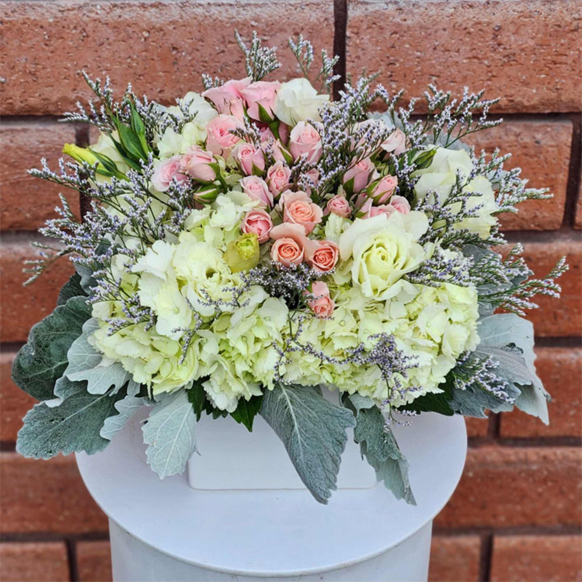 Pink and white rose bouquet with pale hydrangeas in a white container