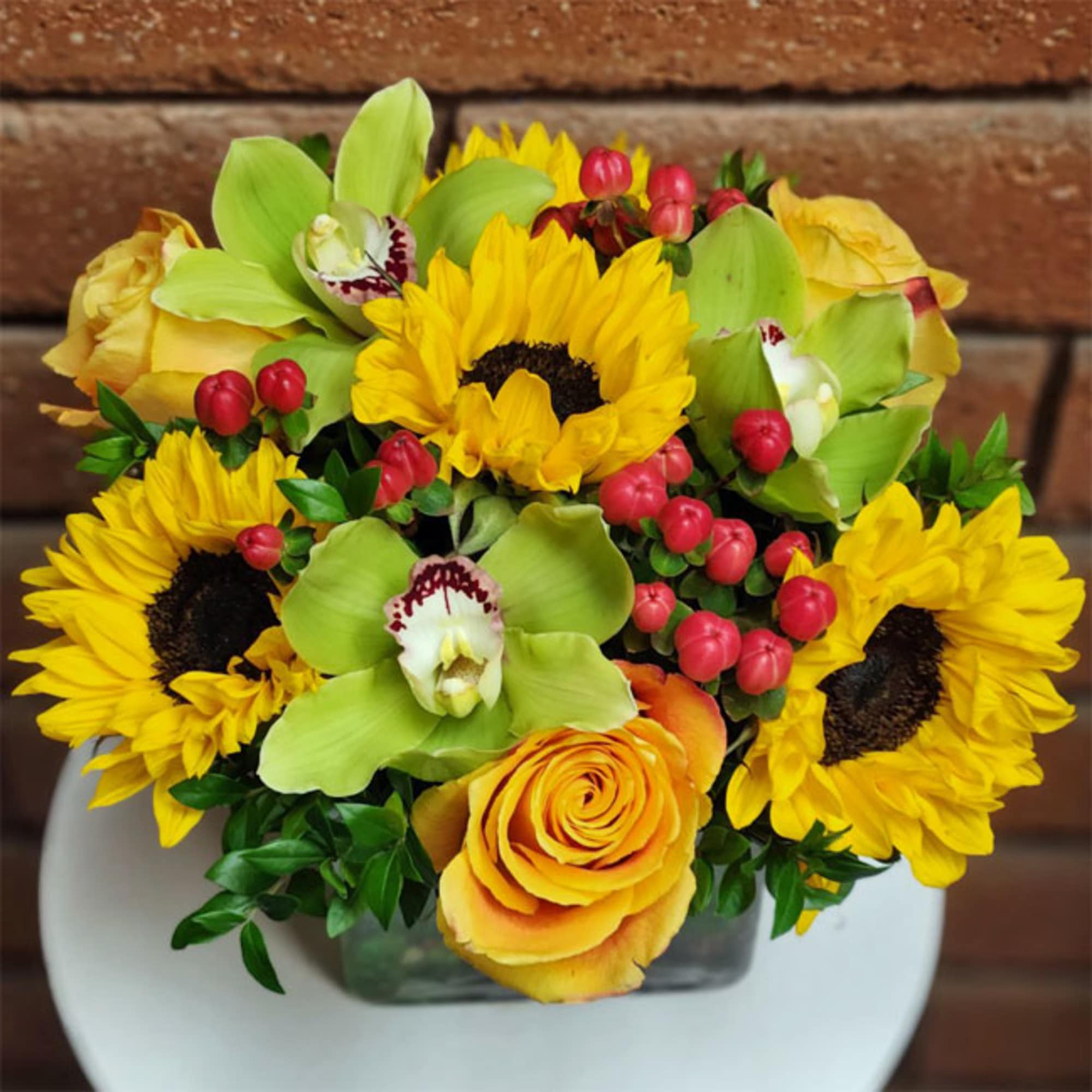 Bouquet of sunflowers, yellow roses, and green orchids in a vase