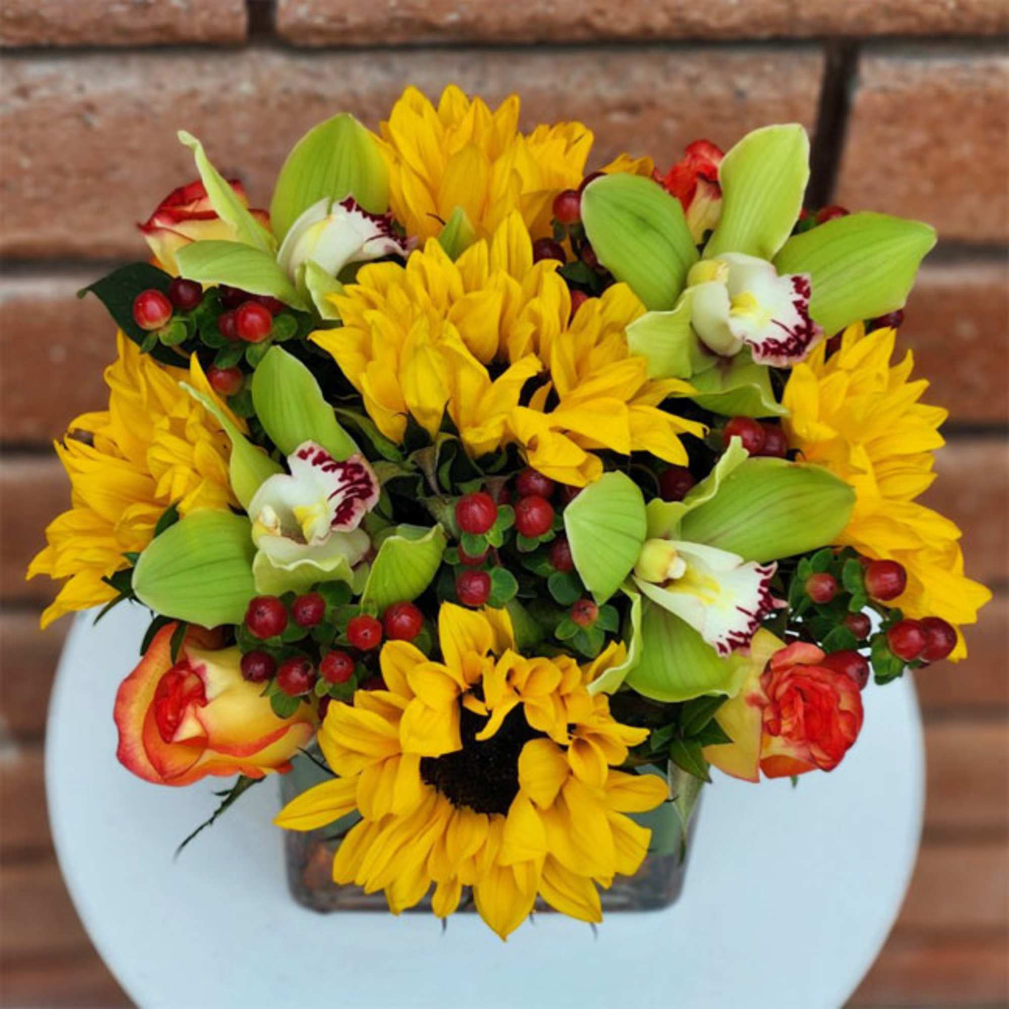 Bouquet of yellow sunflowers and green orchids in a glass vase
