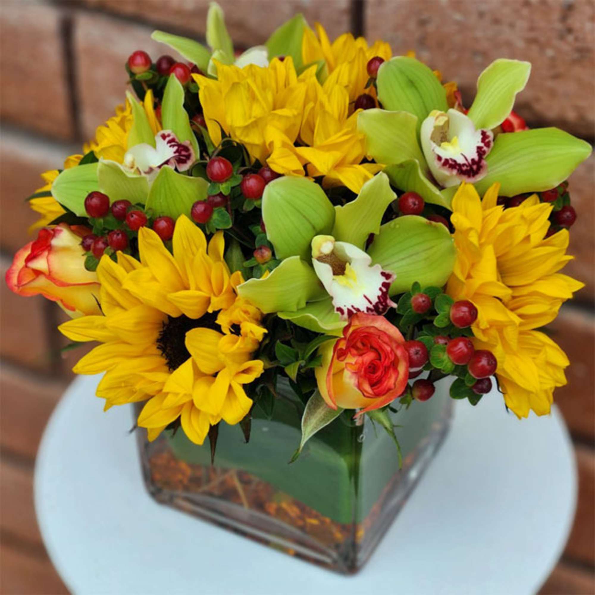 Yellow sunflowers and orchids in a square glass vase
