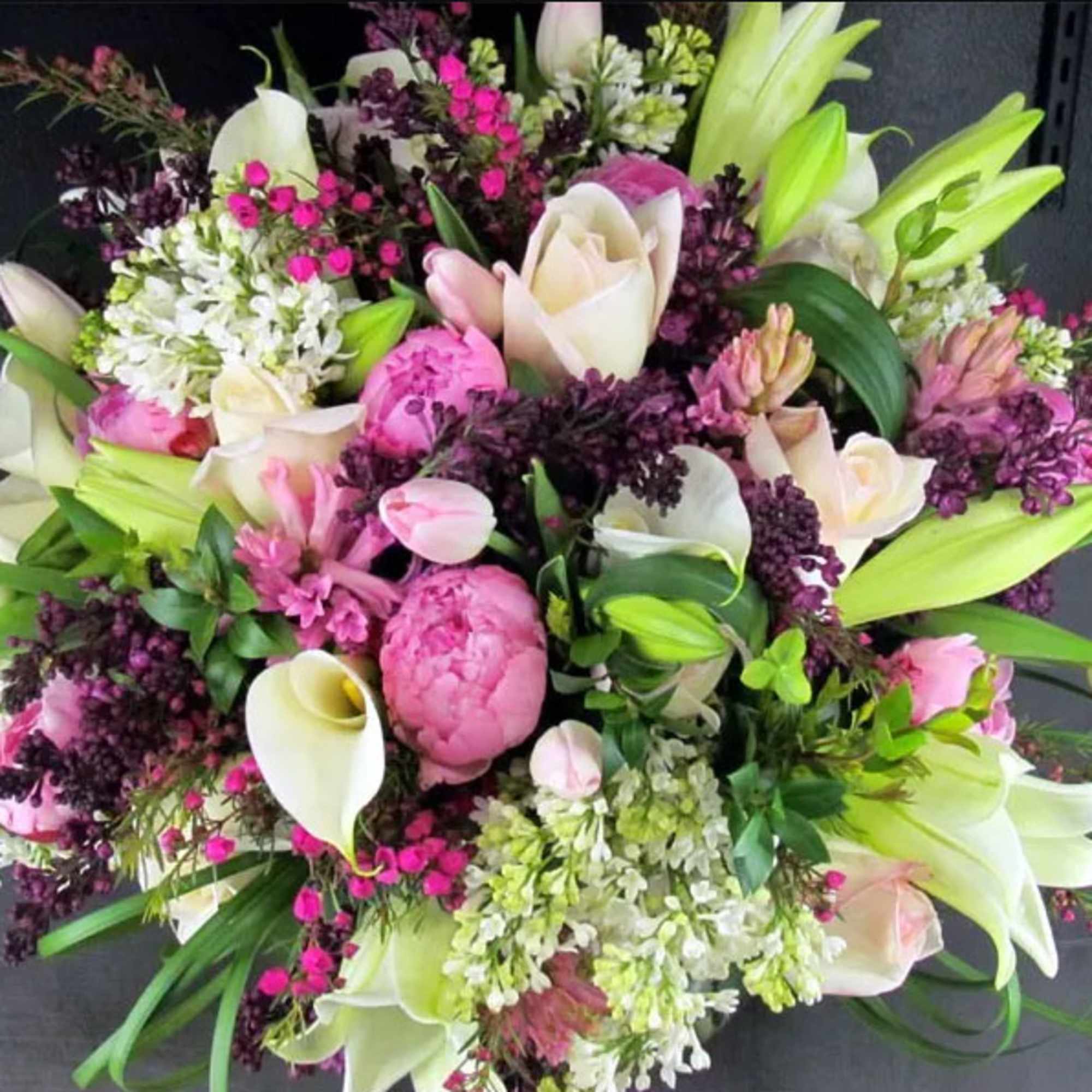 Lush arrangement of pink peonies, white roses, lilies and calla lilies with purple accents