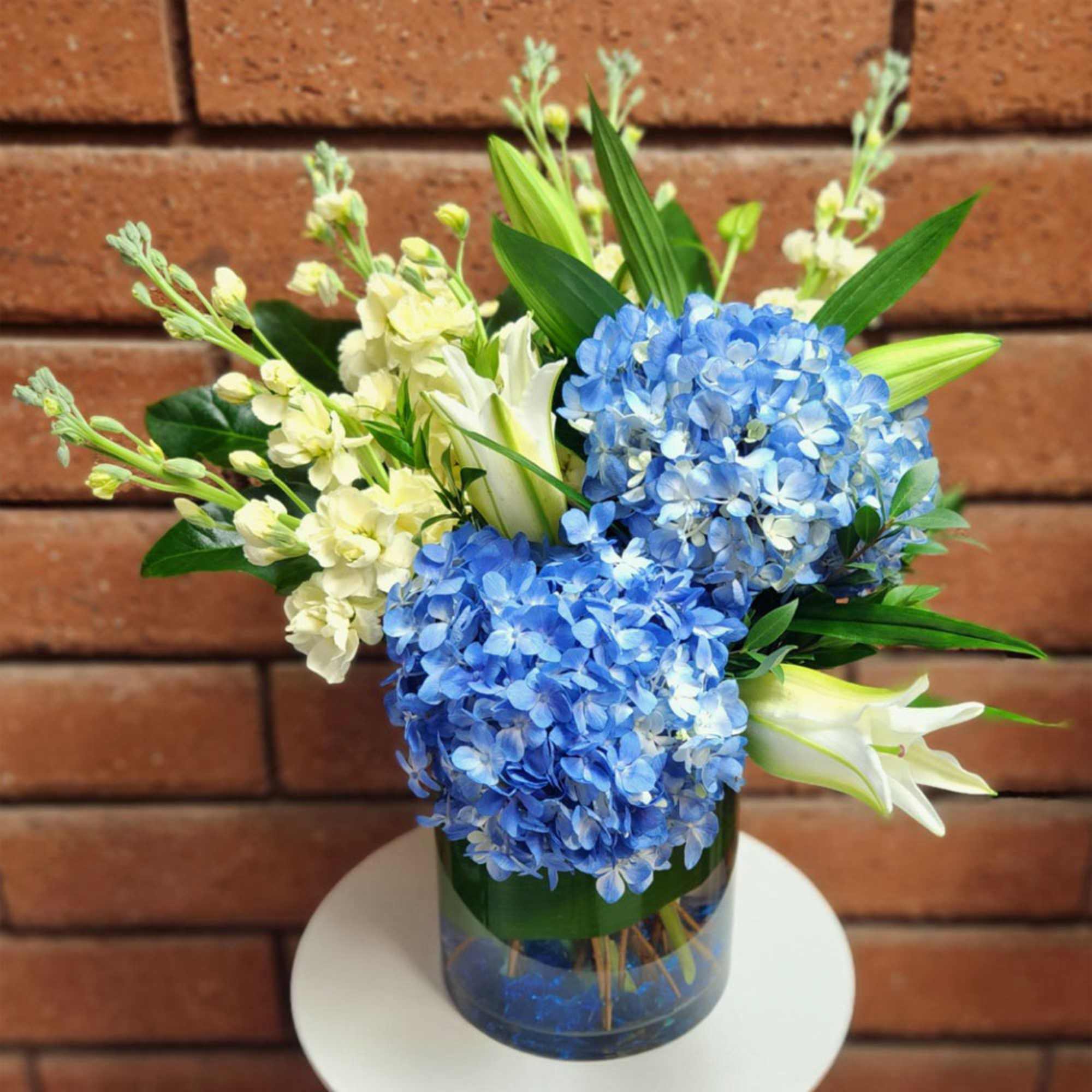 Blue hydrangeas and white lilies in a glass vase