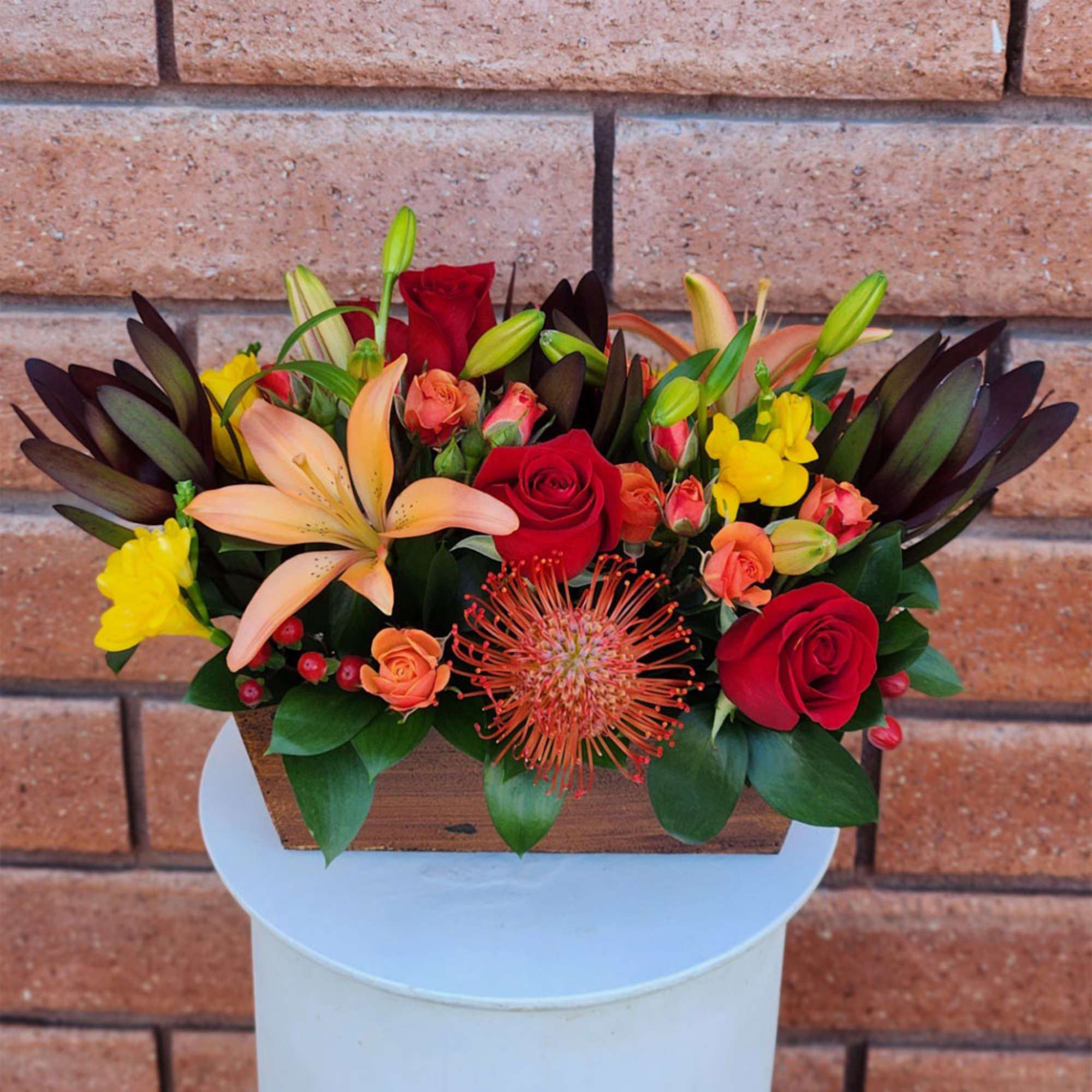 Mixed bouquet with red roses, lilies, and yellow blooms in a wooden container