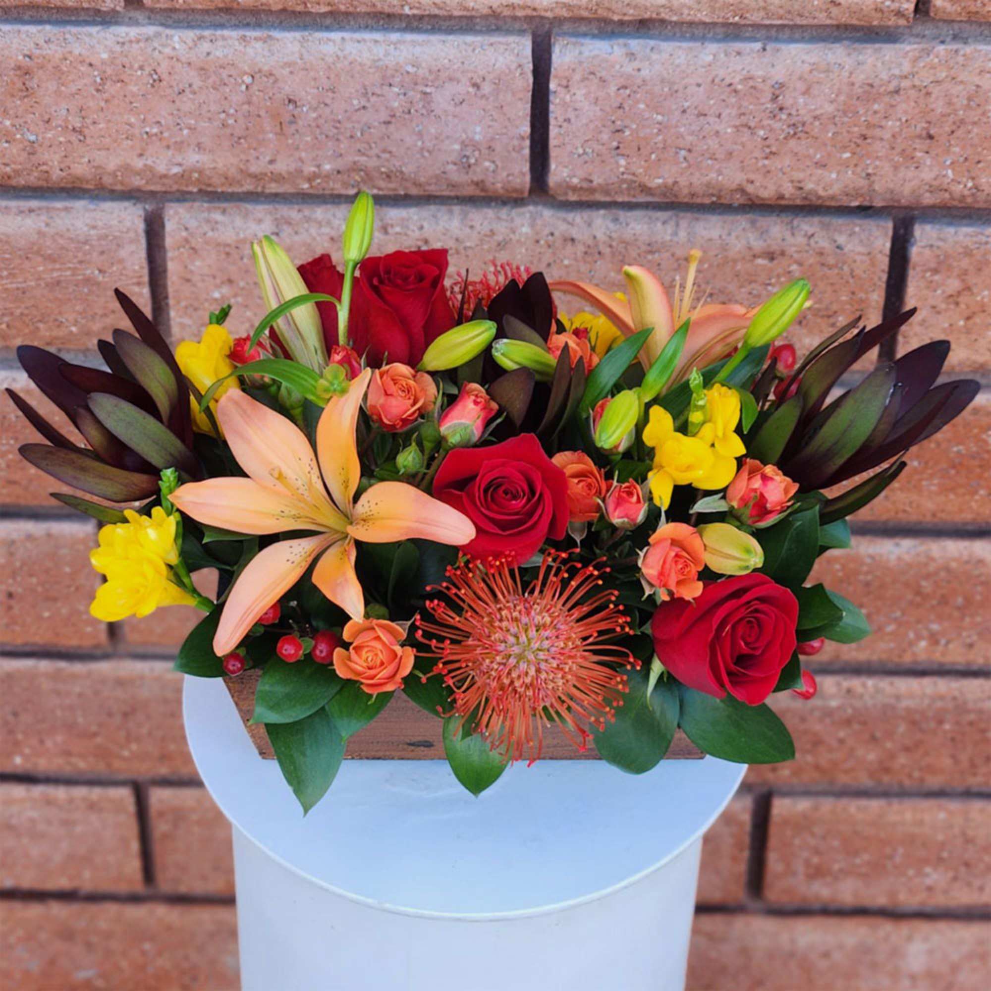 Mixed bouquet with red roses, peach lilies, and yellow blooms in a wooden box