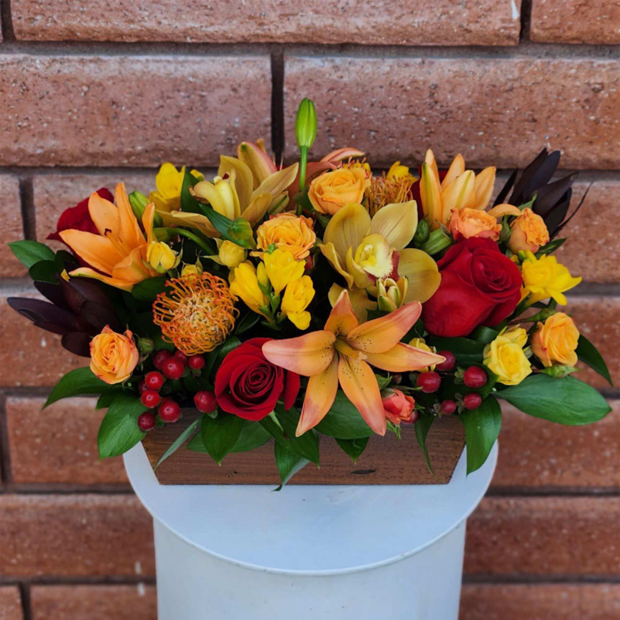 Mixed bouquet of red, yellow, and orange flowers in a wooden container