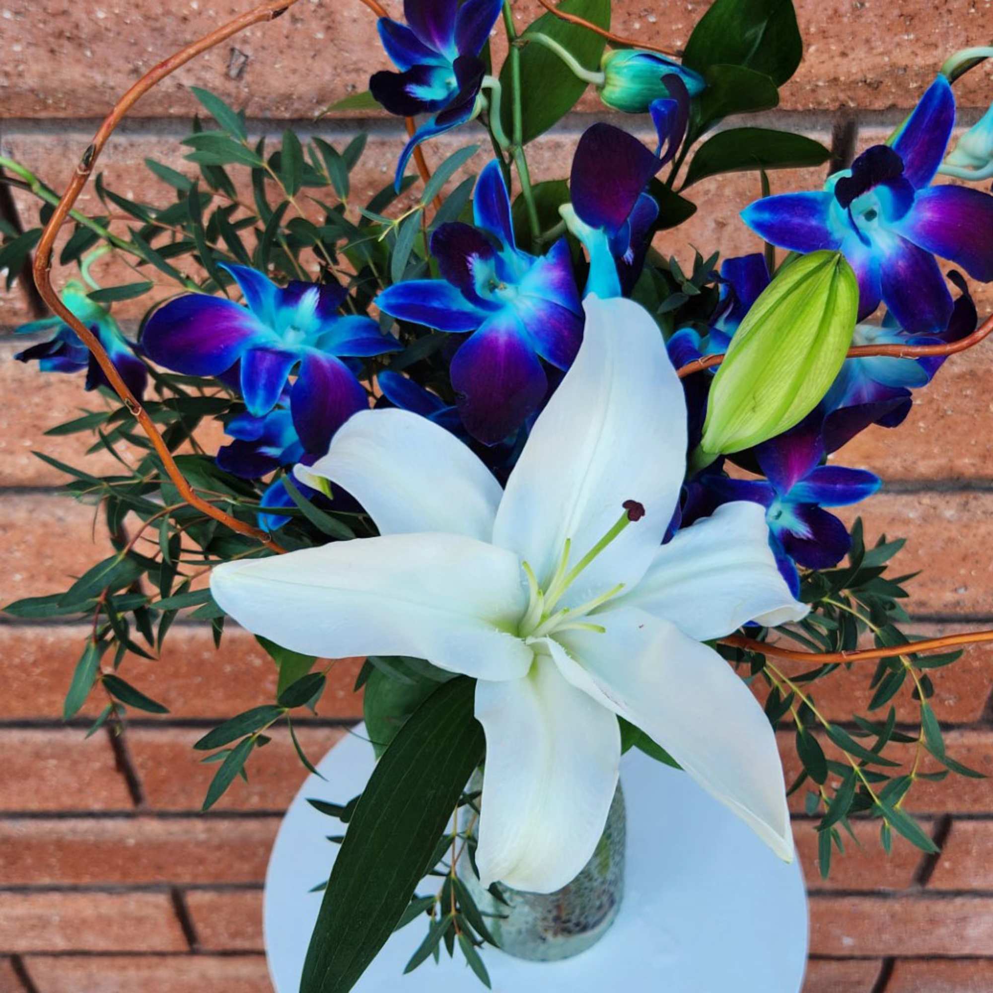 White lily bouquet with blue-purple orchids in a glass vase