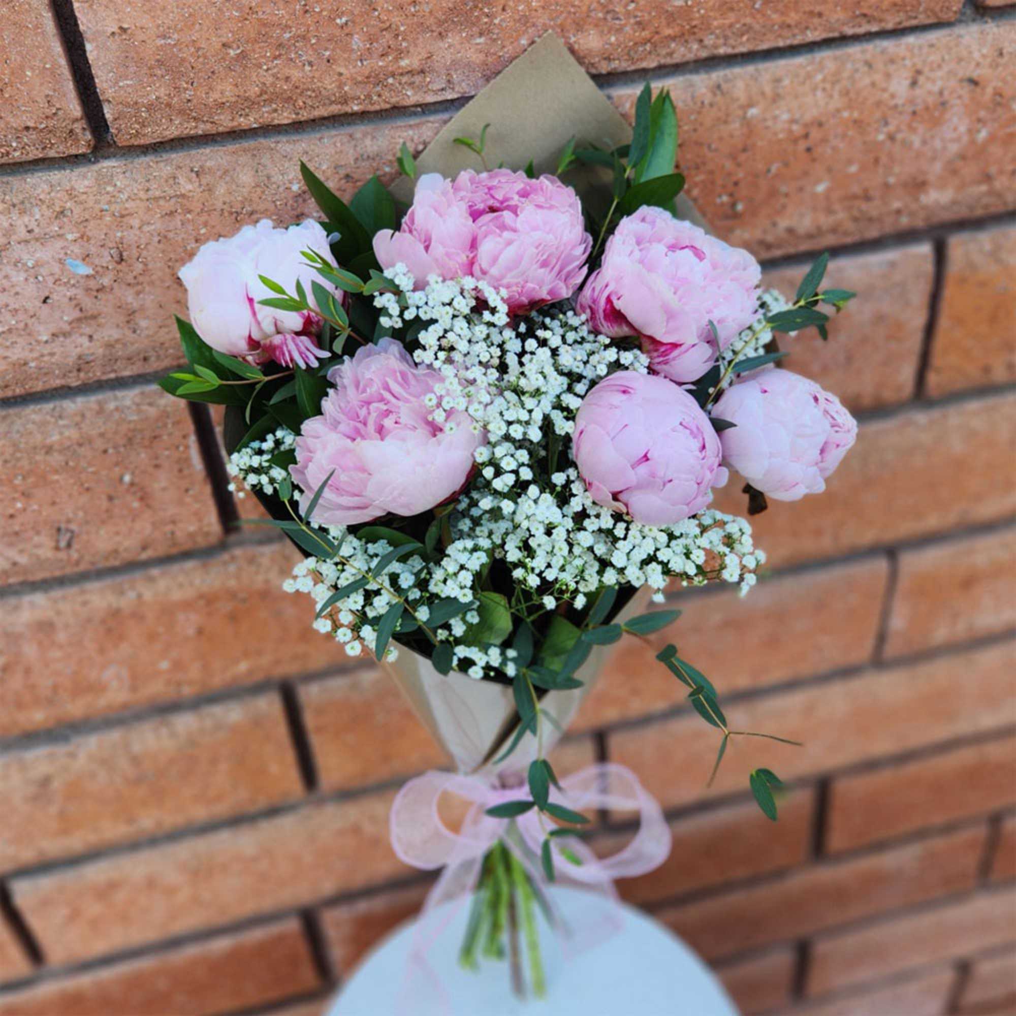 Pink peony bouquet with baby's breath and greenery, wrapped in paper and tied with ribbon