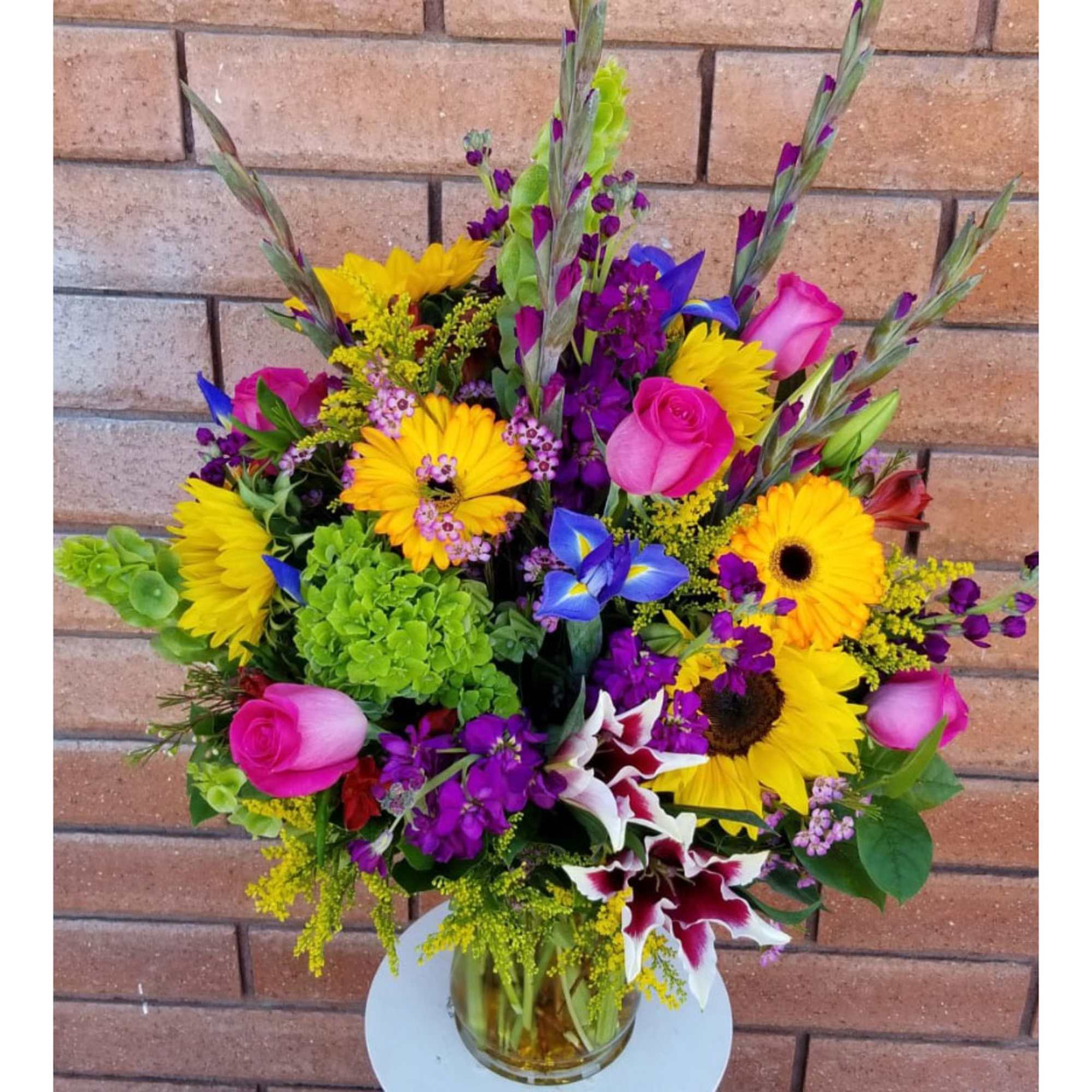 Colorful mixed bouquet with roses, sunflowers, and purple flowers in a glass vase