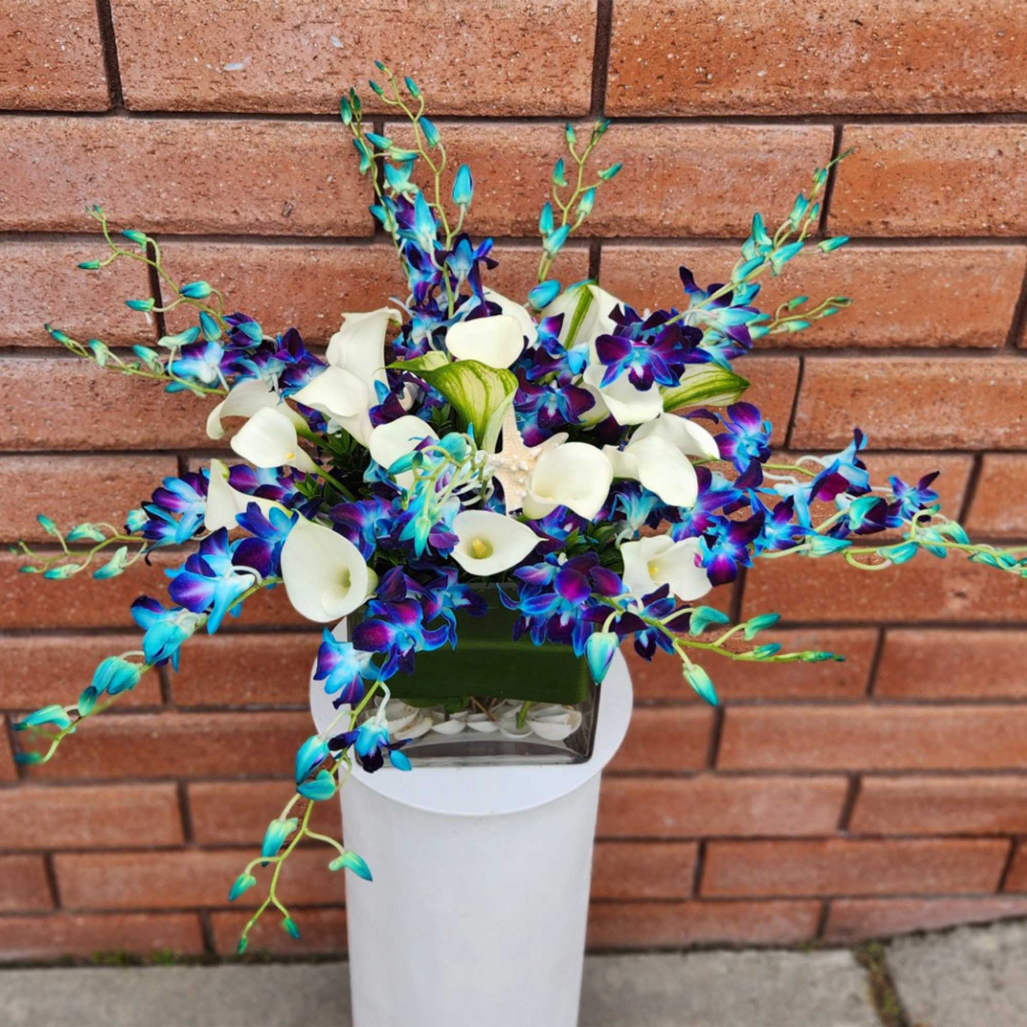 Blue and white orchid arrangement in a square glass vase