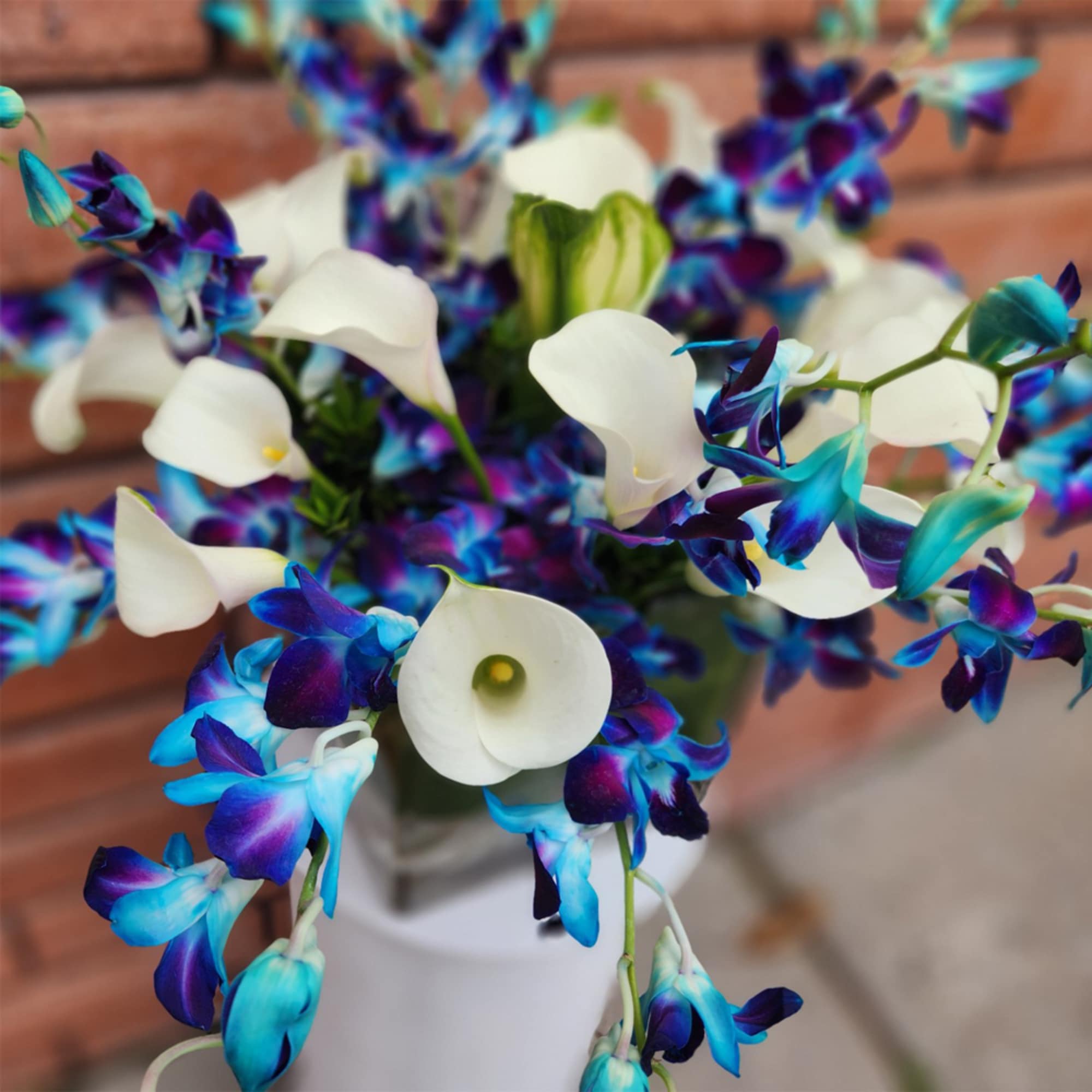 Bouquet of white calla lilies and blue-purple orchids in a white vase