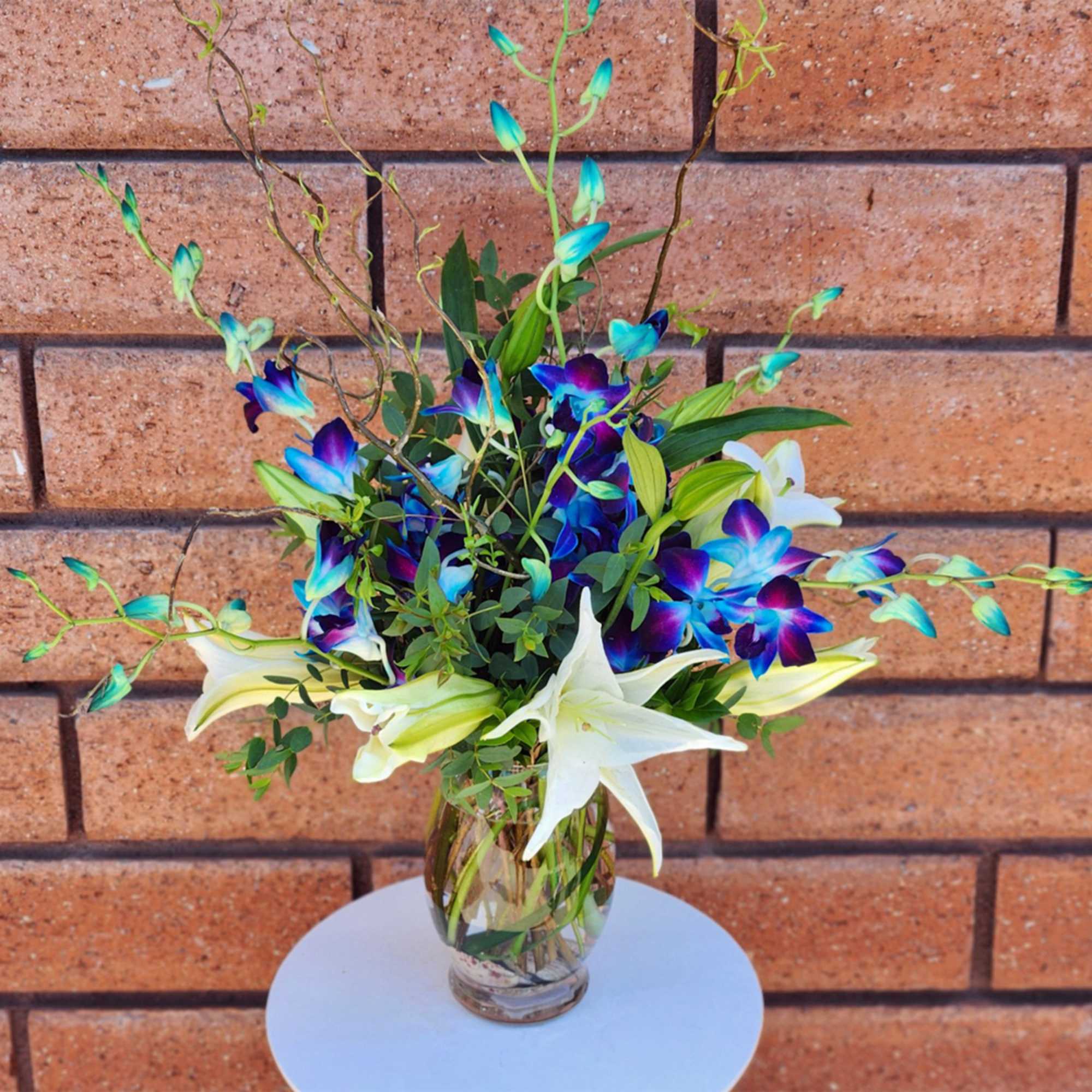 Bouquet of white lilies and blue-purple orchids in a glass vase