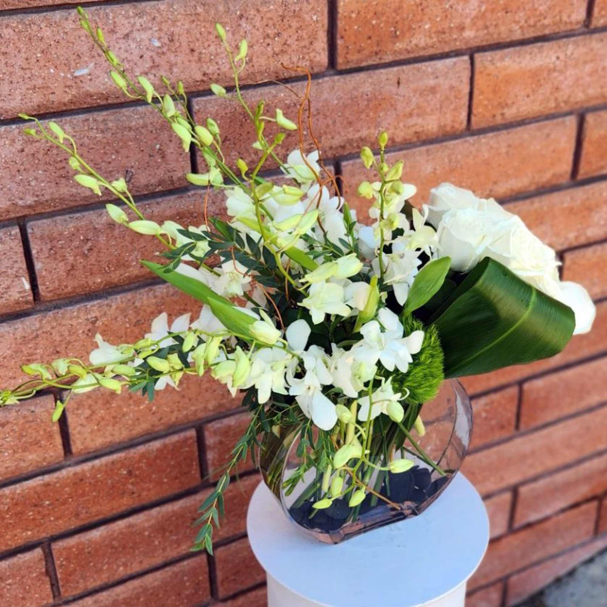 White floral arrangement in a clear glass vase with long green stems
