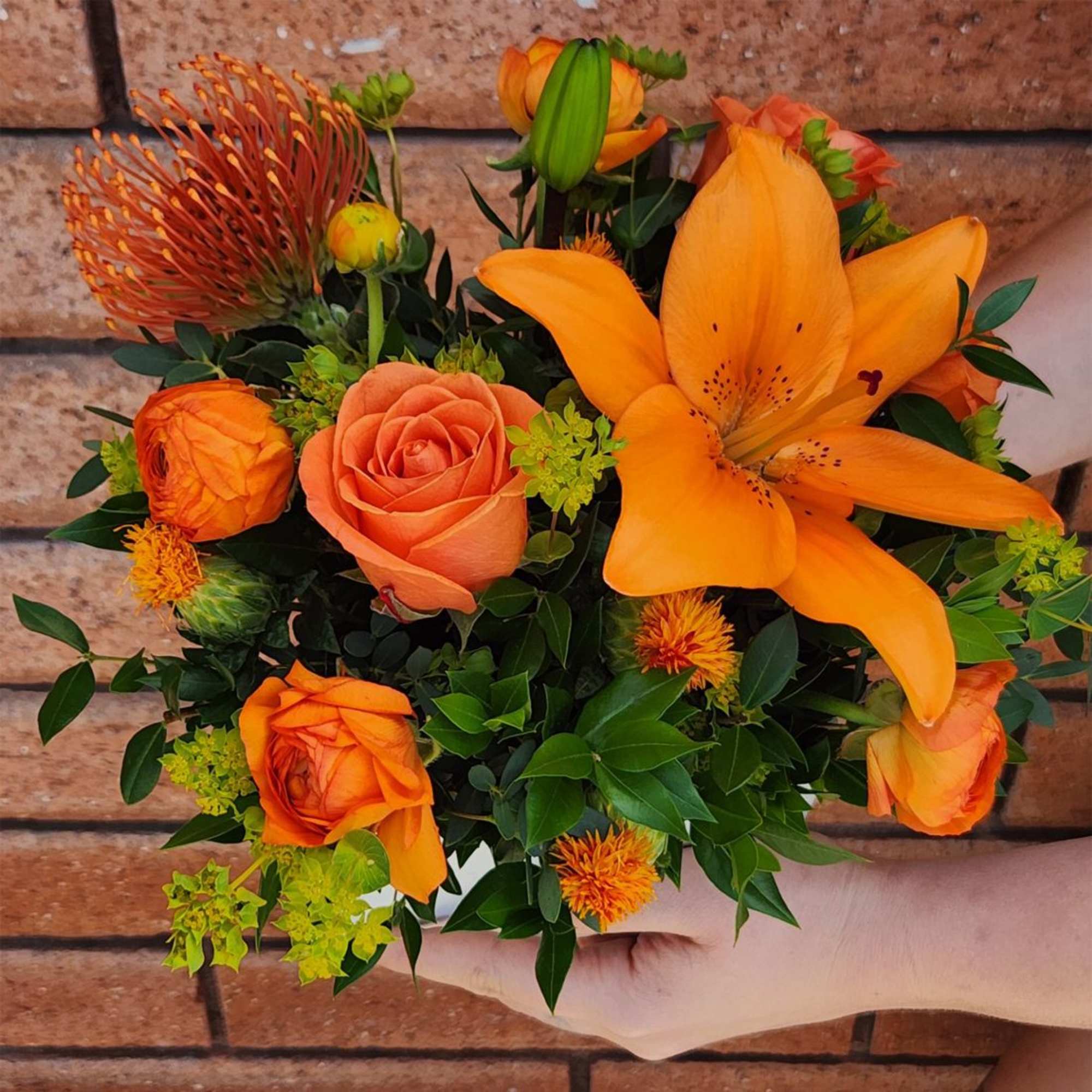 Orange bouquet with roses and a lily held in hand